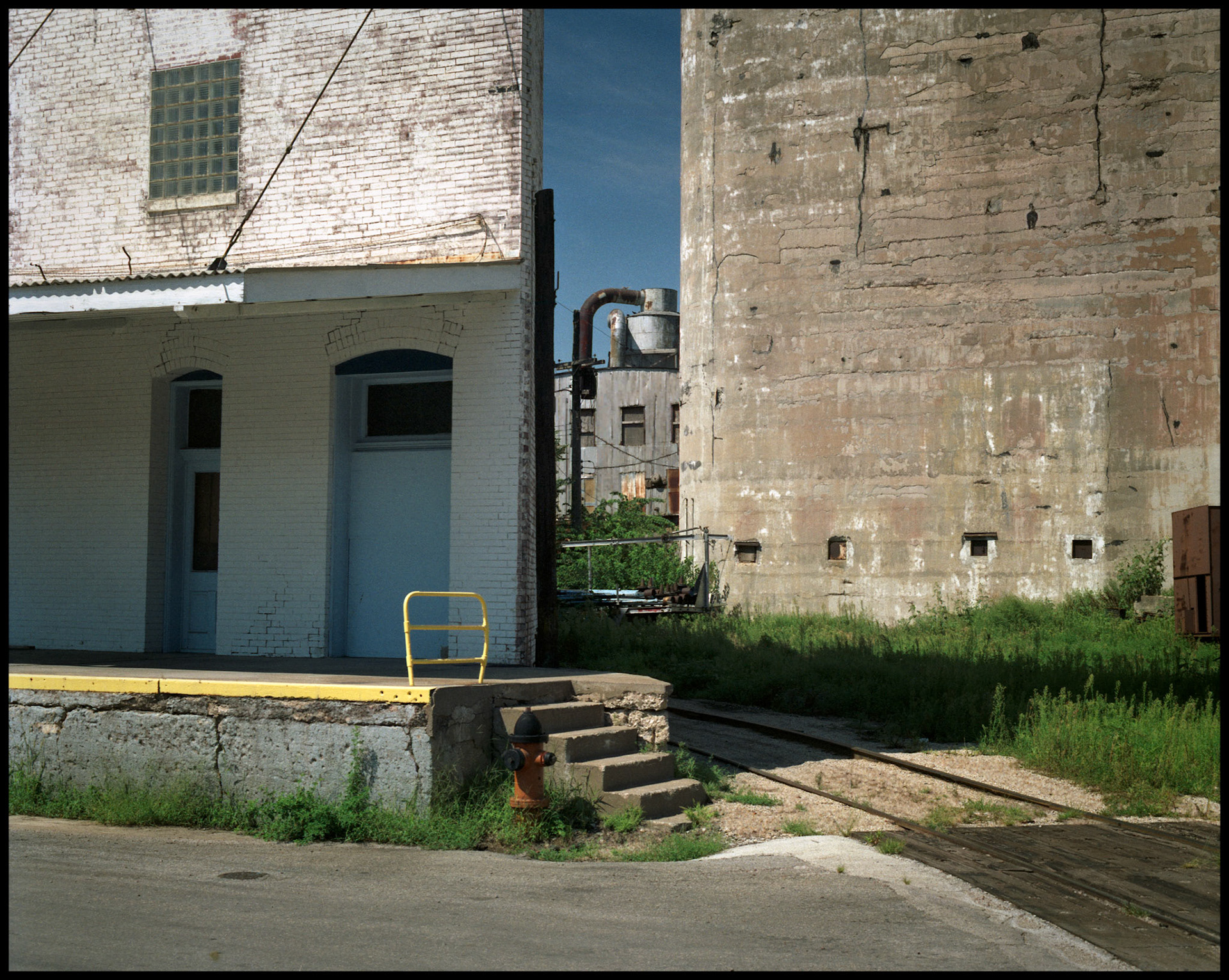 Cityscape of a loading dock and railroad track curving between two industrial buildings. Kansas City, Missouri, 1990