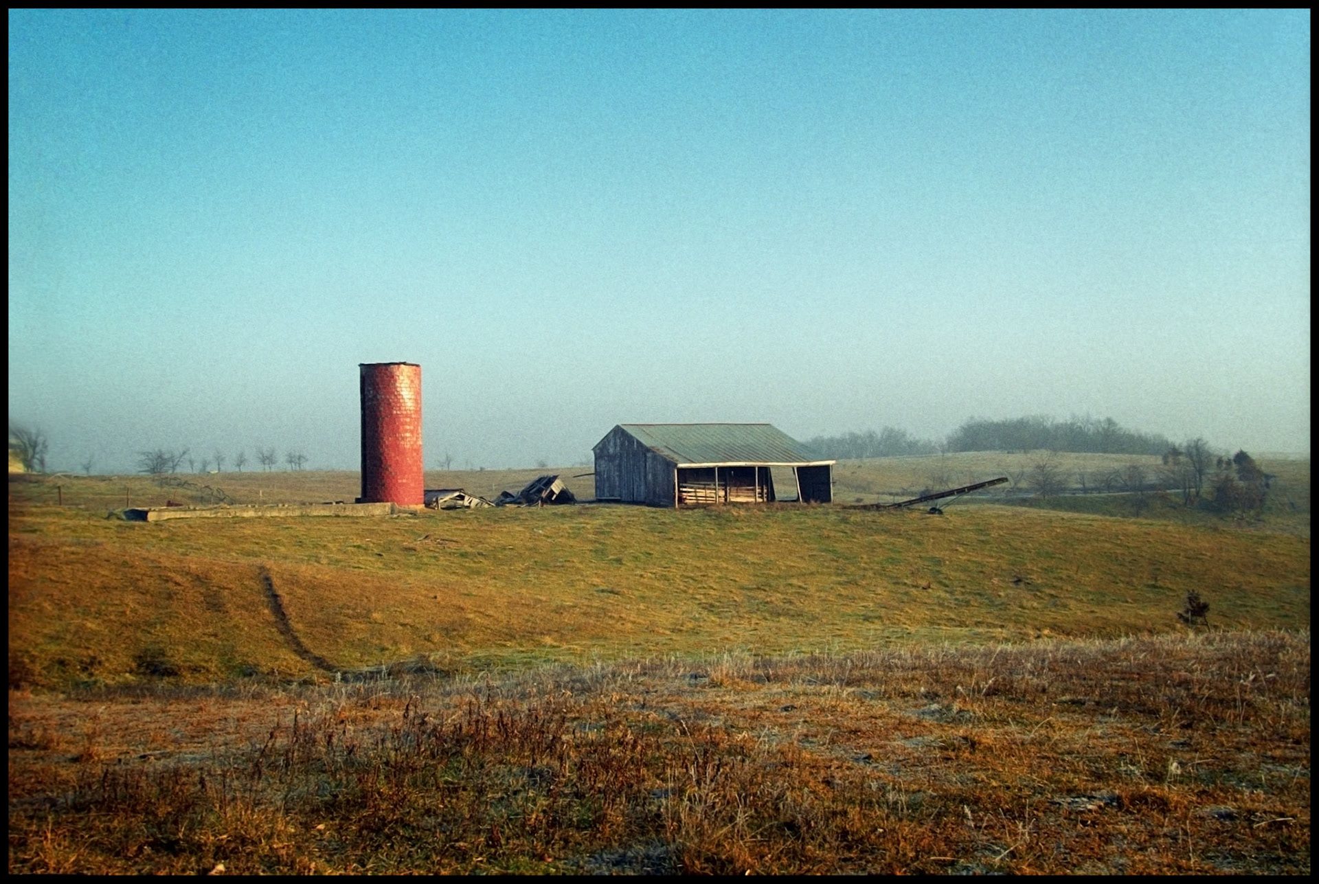 A barn and red brick grain silo on a hillside on a misty morning. Near Pure Air, Missouri, 1994.
