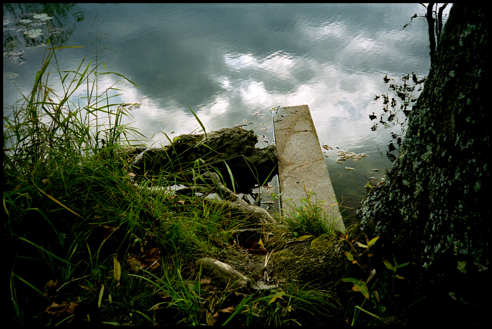 A flooded cement wall at the edge of a lake that appears to be a walk that leads to the "heavens" of the cloud reflection as a sort of "Port of Entry". Falling Springs Mill, near Winona, Missouri in the Missouri Ozarks, 1991.