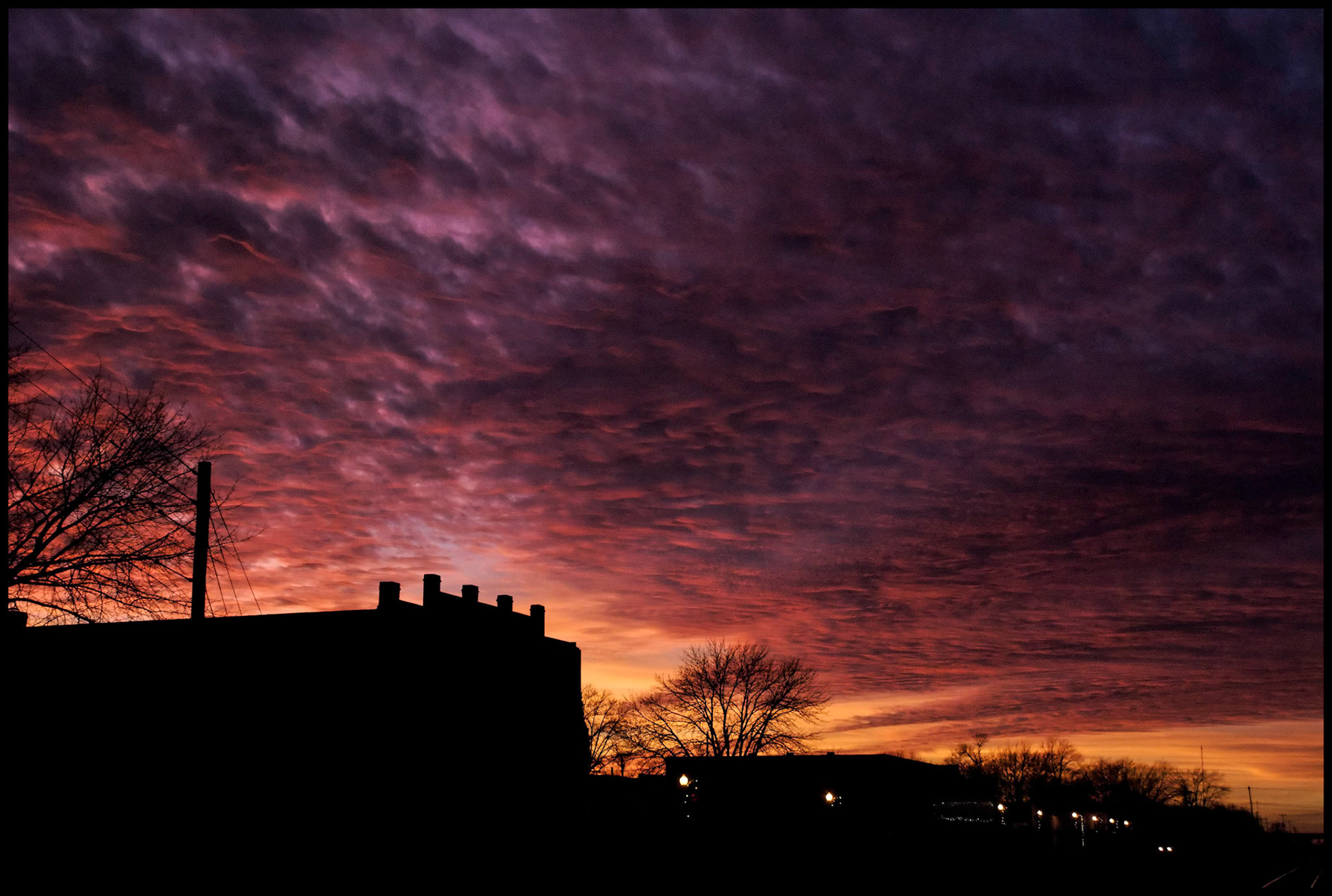 Textured Orange and Pink clouds at sunset behind silhouetted downtown Centralia, Missouri buildings with row of streetlamps in foreground. 2008