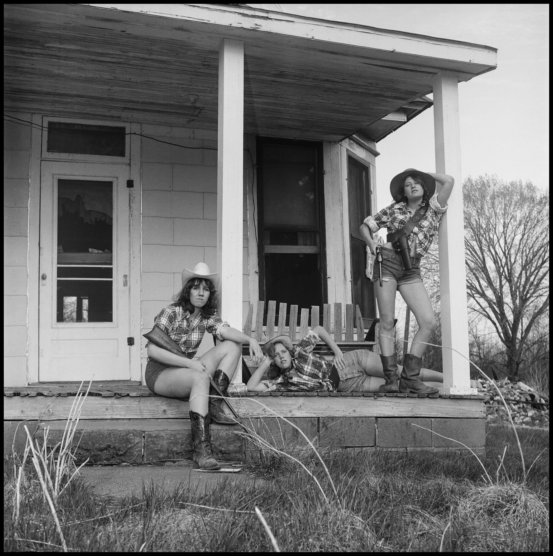 A vintage image of three teenage girls posing as hillbilly cow girls with props in front of an abandoned house. Kirksville Missouri 1978