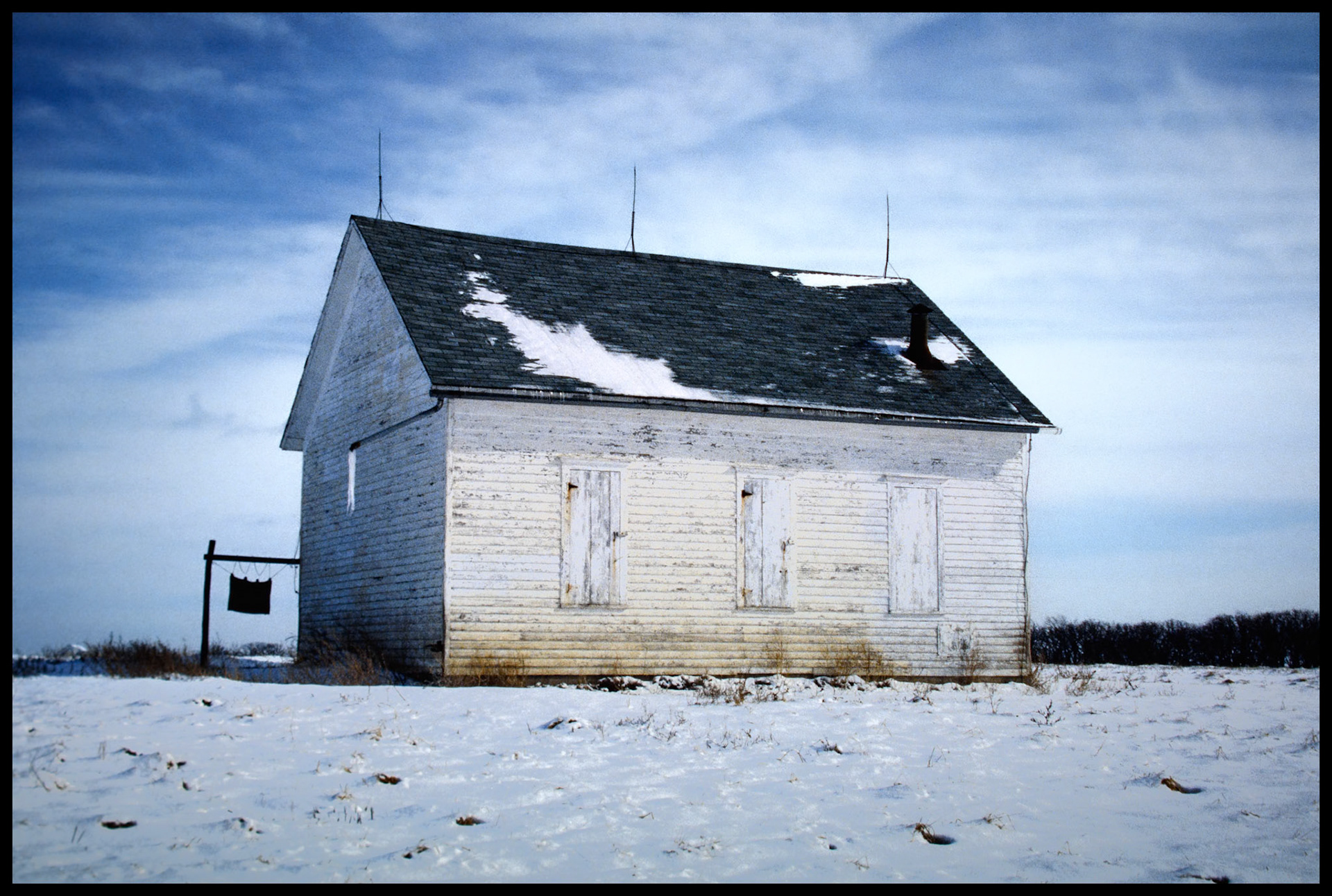 A partially snow covered abandoned rural schoolhouse converted to a farm building with a large icicle hanging from it's gutter drain pipe. This was the former Maple Grove schoolhouse near Pure Air in Adair County, Missouri, which was closed in 1953 and later purchased and moved to a nearby farm. This was one of 76 rural schoolhouses in Adair county through the mid 20th century. 1985