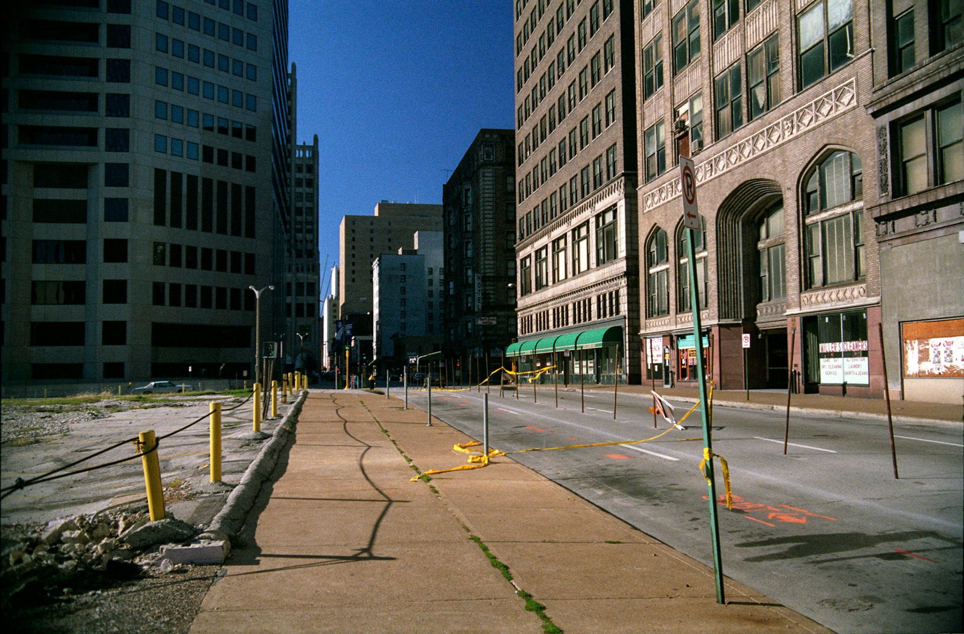 St. Louis Urbanscape of deserted street with yellow tape and sidewalk with side lit buildings in distance. Part of a series shot one afternoon in November, 1988 called An Afternoon in St. Louis (a subset of my Industrial Geometry series).