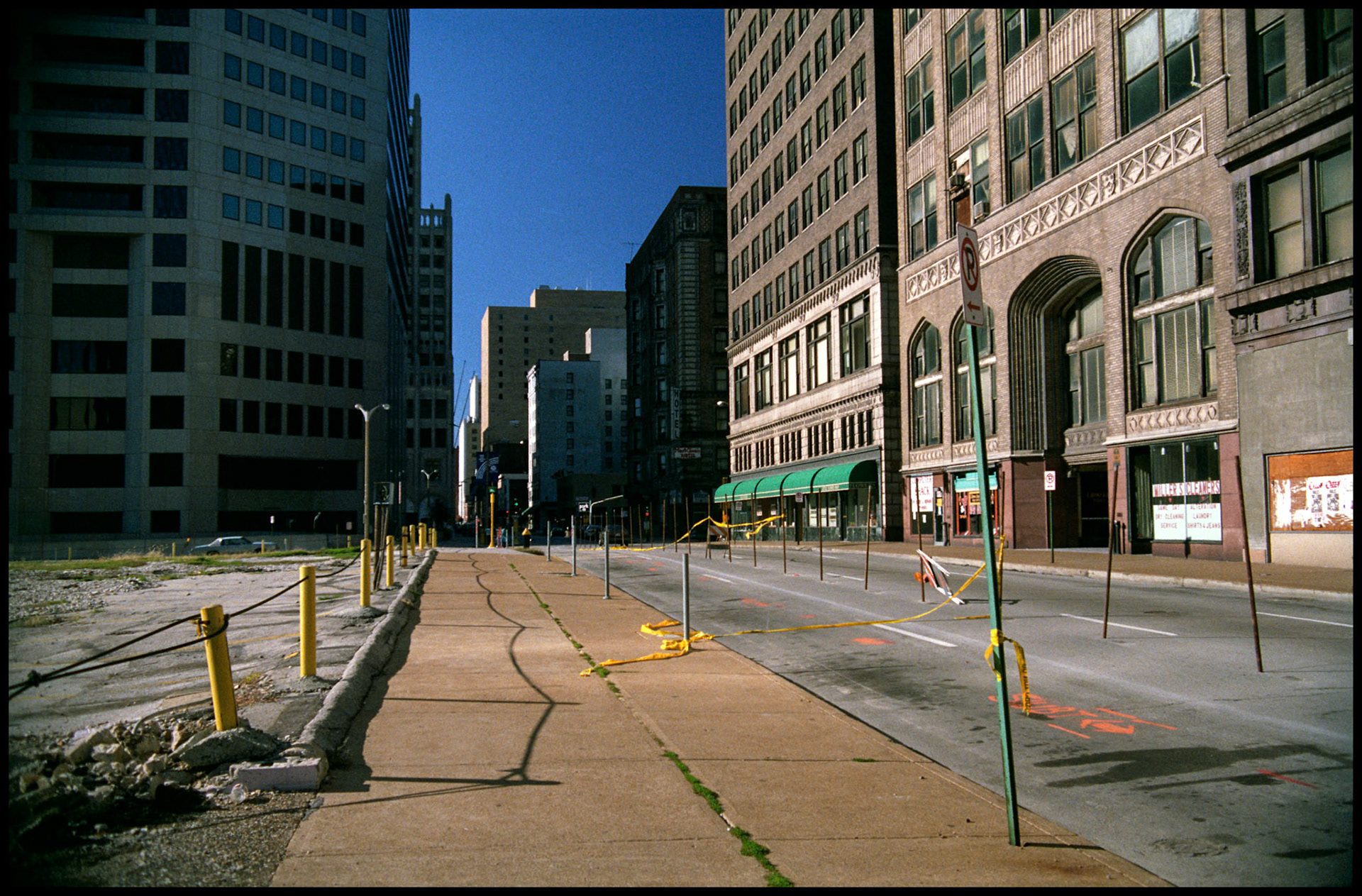 St. Louis Urbanscape of deserted street with yellow tape and sidewalk with side lit buildings in distance. Part of a series shot one afternoon in November, 1988 called An Afternoon in St. Louis (a subset of my Industrial Geometry series).