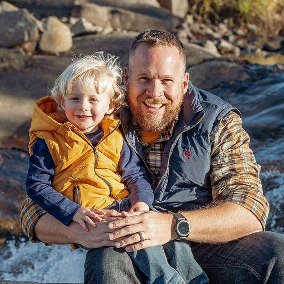 Photographer Ashley Bell and his son sitting on a rock smiling