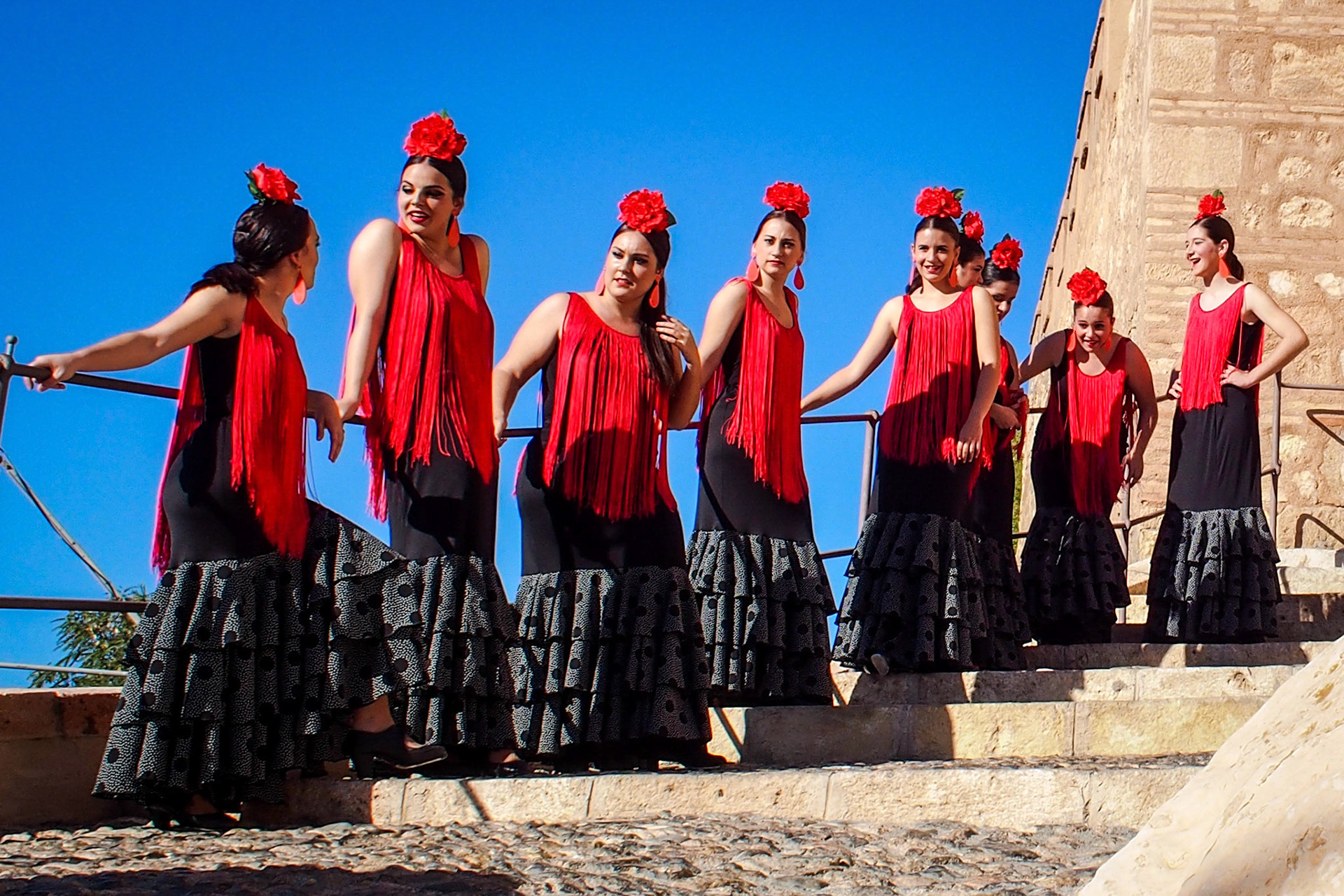 A row of girls in traditional flamenco dress wait on the steps of the Alcazaba in Almeria City in spain.