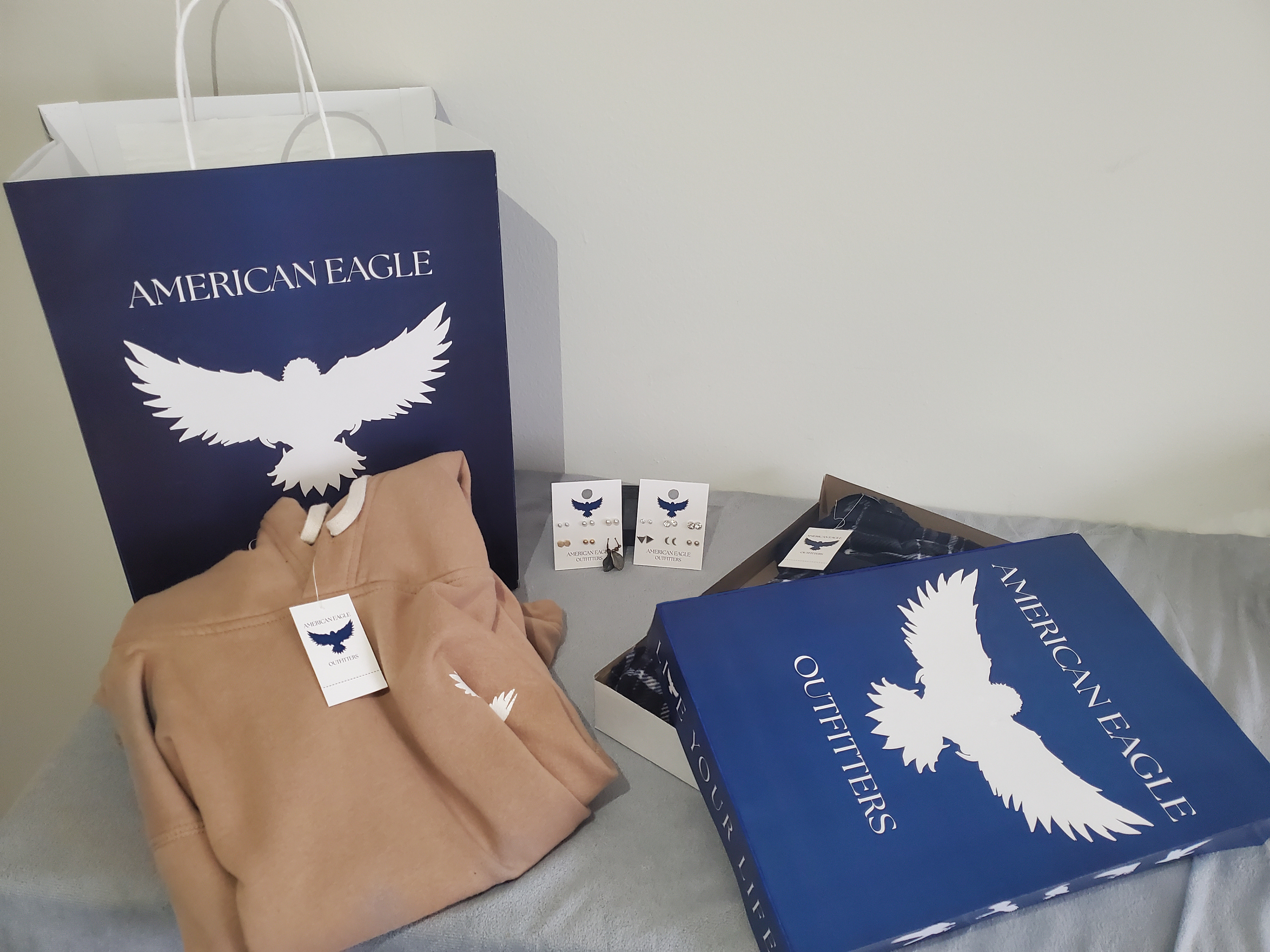 Completed photoshoot with hang tag, price tags, shirt box, and shopping bag, accompanied with a sweatshirt, earrings, and sweatpants.