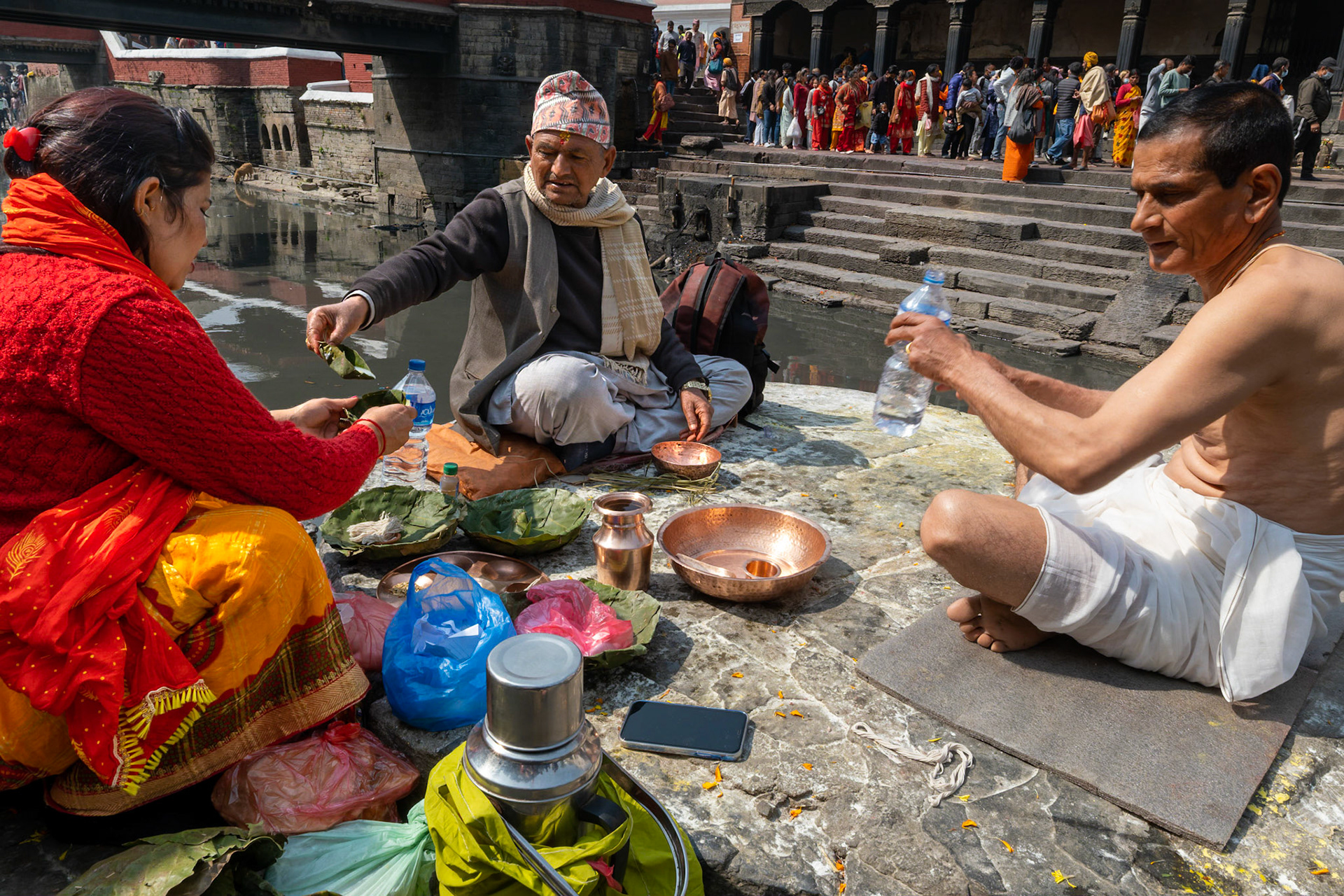 En face de la file d'attente qui s'étend indéfiniment, un curieux rite se déroule. Il semble qu'un novice viennent s'initier auprès d'un ancien aux rites de l'offrande.