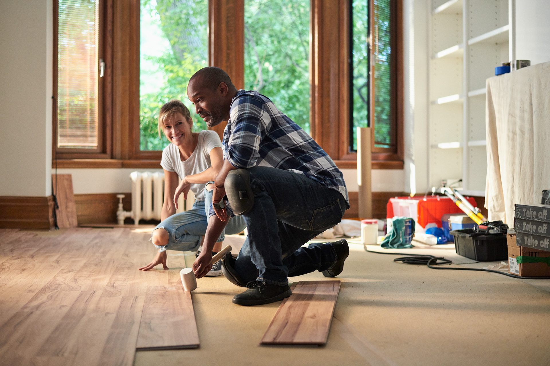 young mixed race couple installing a floating floor in their new apartment building, building & construction tools are seen in the background