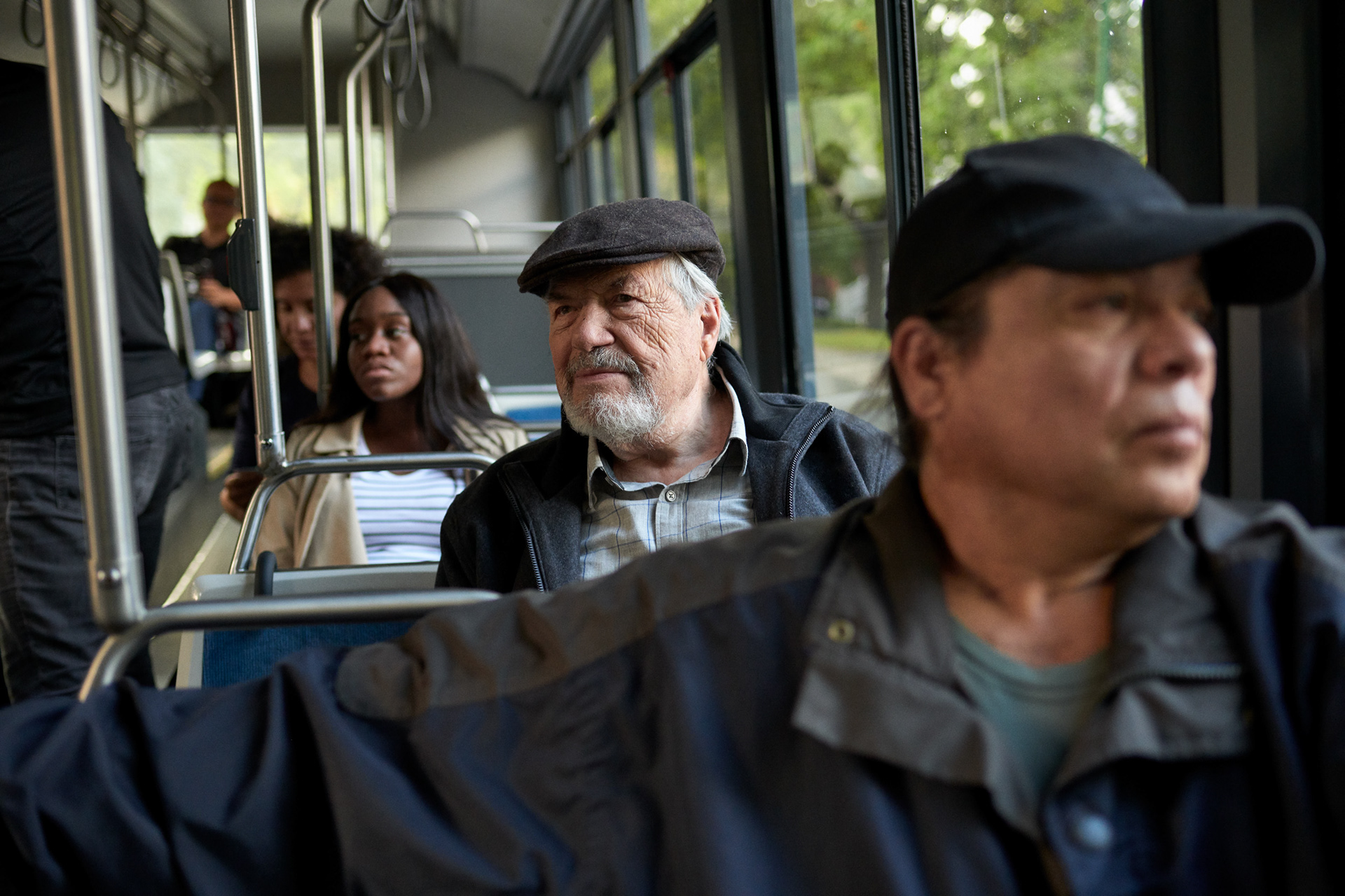 an older gentlemen on a public transport bus is looking up and smelling at other passengers