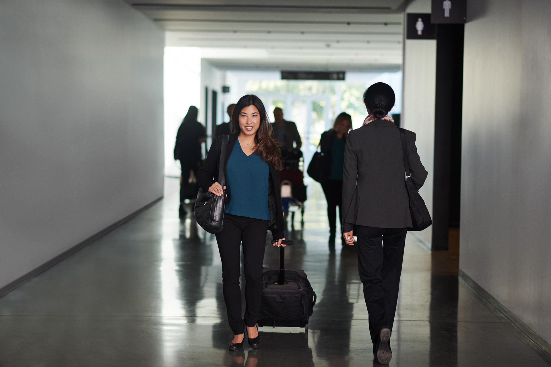 asian woman walking though a photography set designed to look like an airport.  she looks up to the camera while passing another traveller heading to her gate.