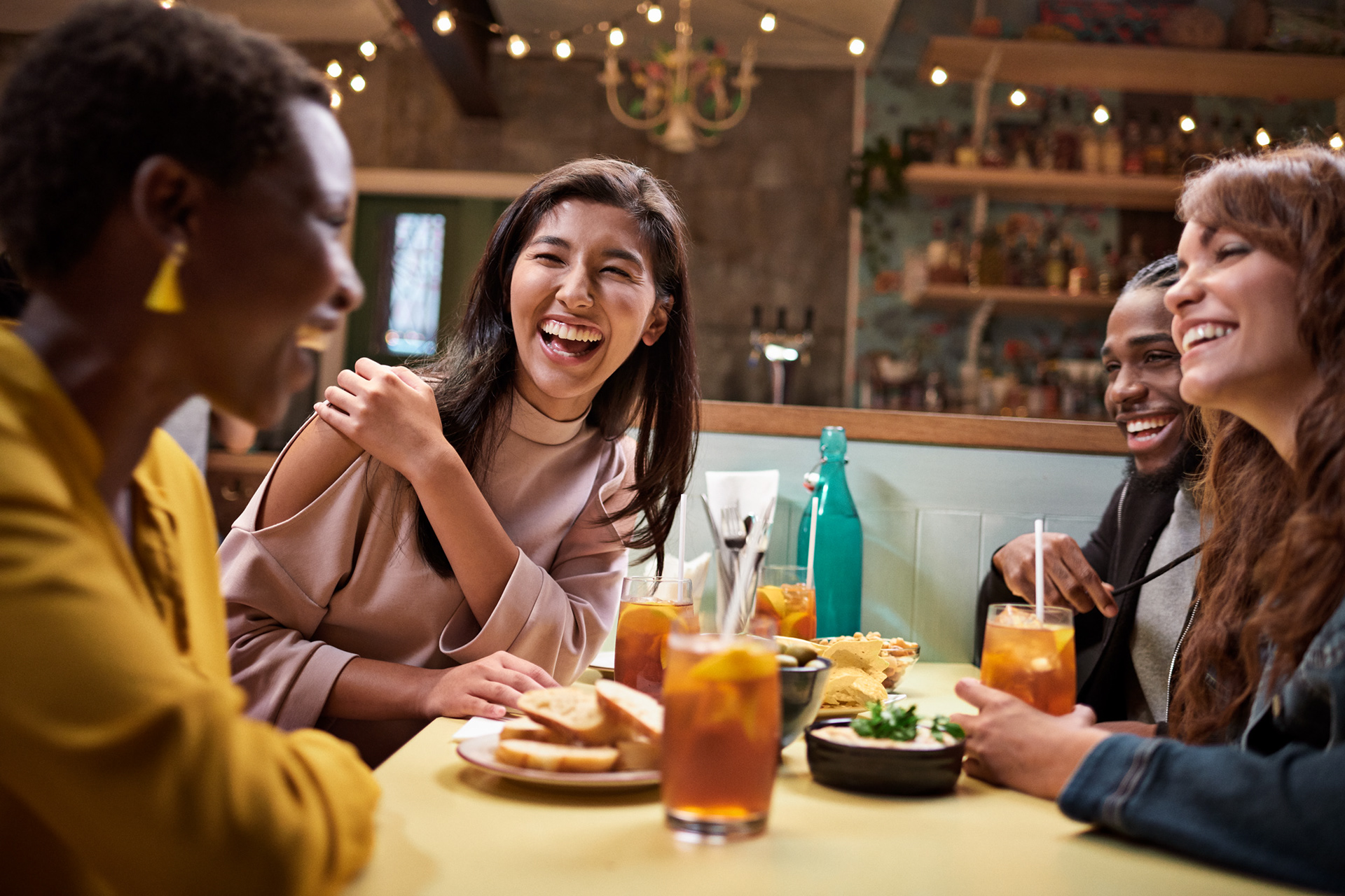 young adults having a fun time out with friends at a local restaurant. they are sharing laughs, food and some drinks.
