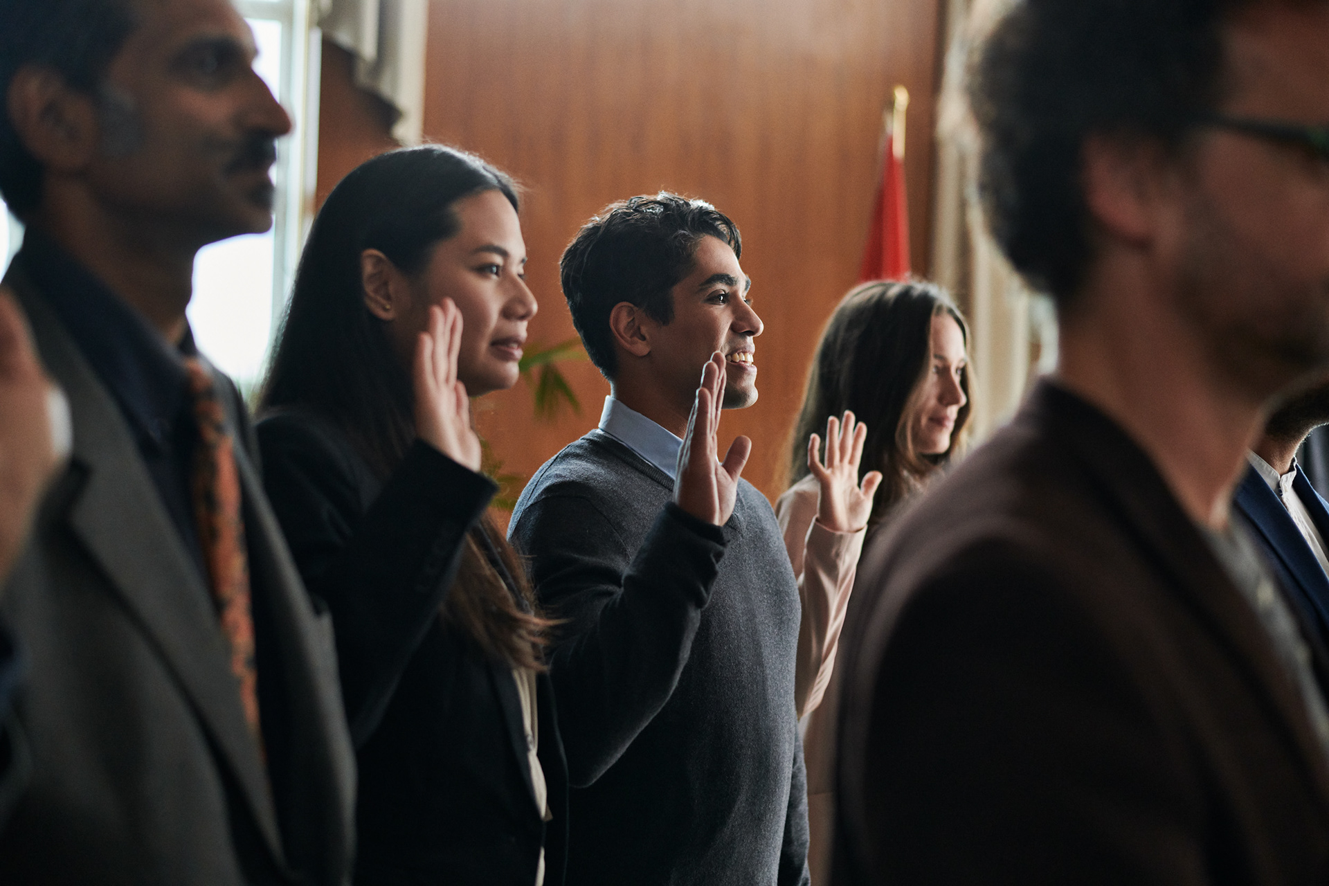 you man and other new immigrants going through a ceremony of becoming a new citizen of canada with the canadian flag i the background.