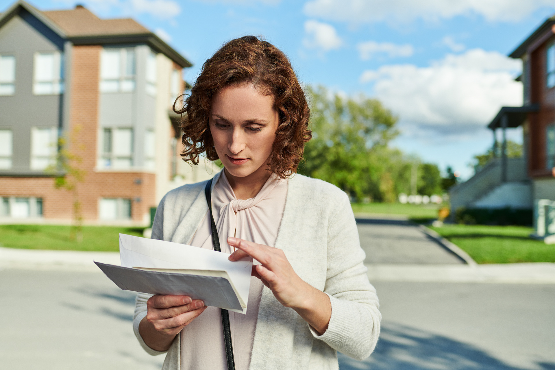 an urban redhead female goes though various letter looking for the one note she is waiting for by a busy roadside in a new devolopement