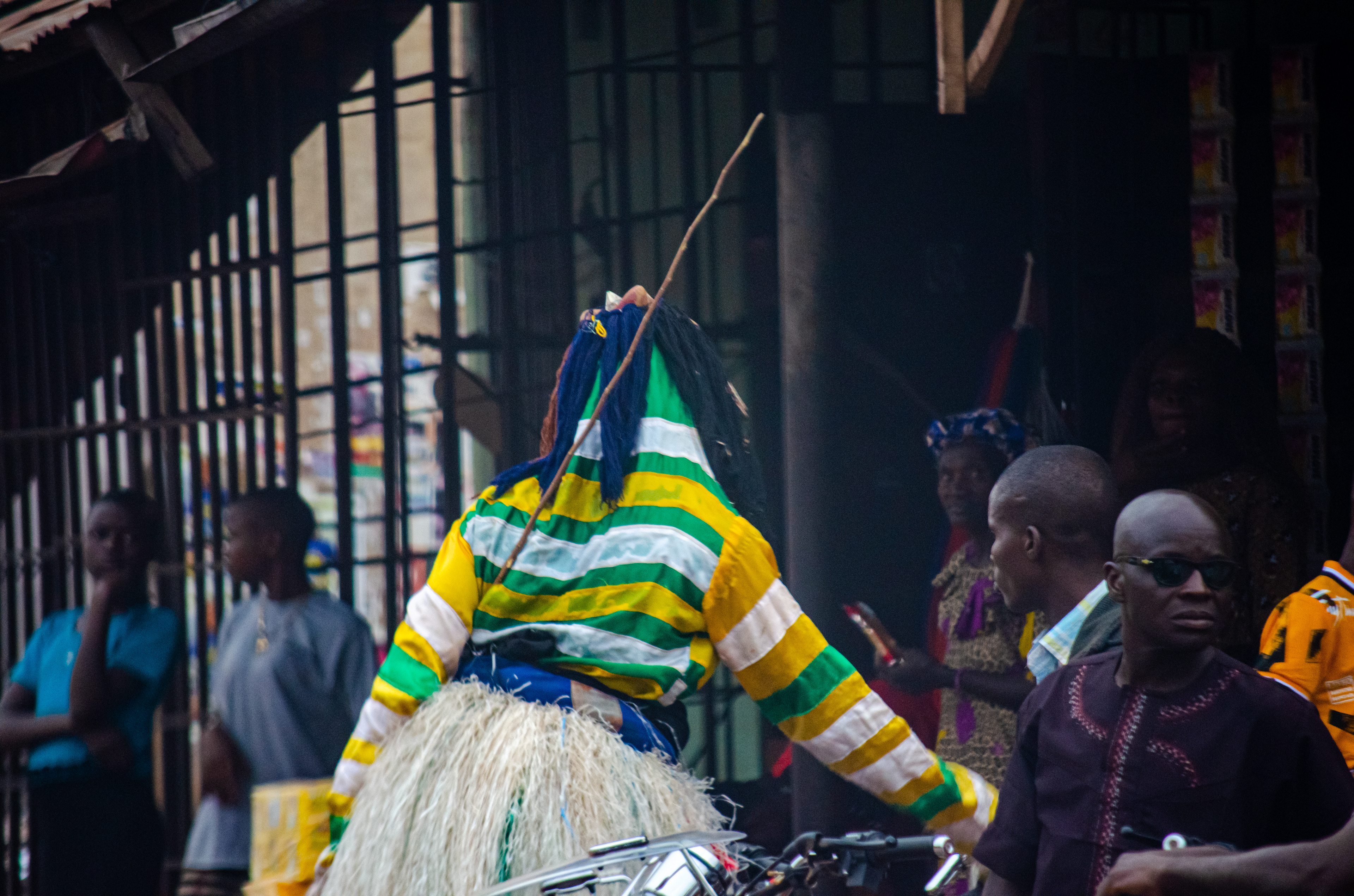 In this picture the masquerade is walking into a shop to either dance for the owners or harass them.
