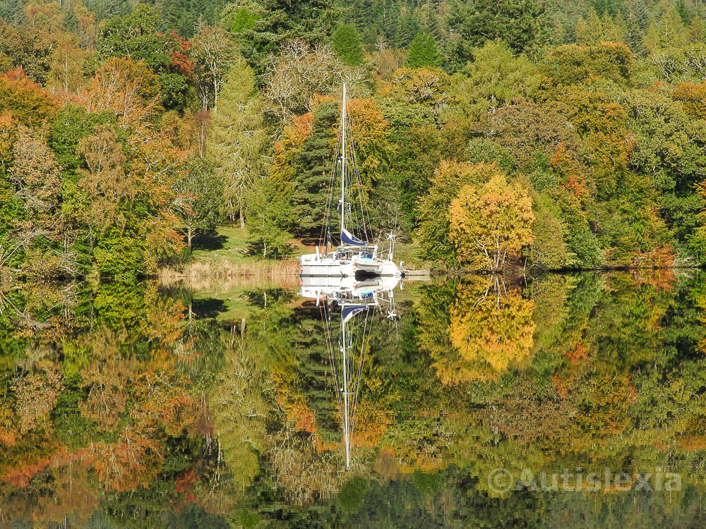 Mirror image of boat and trees in still water on the Caledonian canal