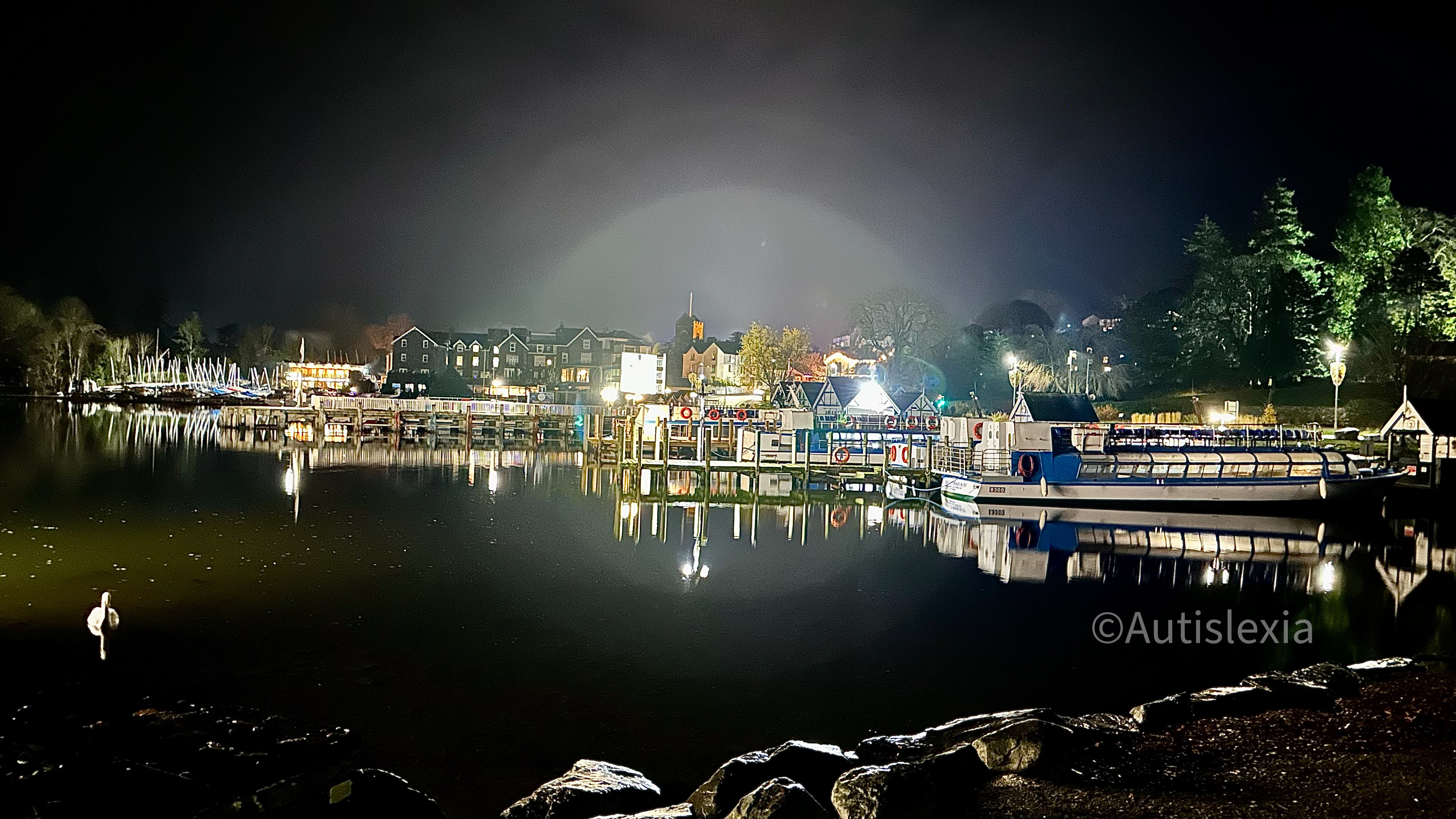Image of Lake Windermere shore at night, with boats tied up and lights creating a circular haze over the image.