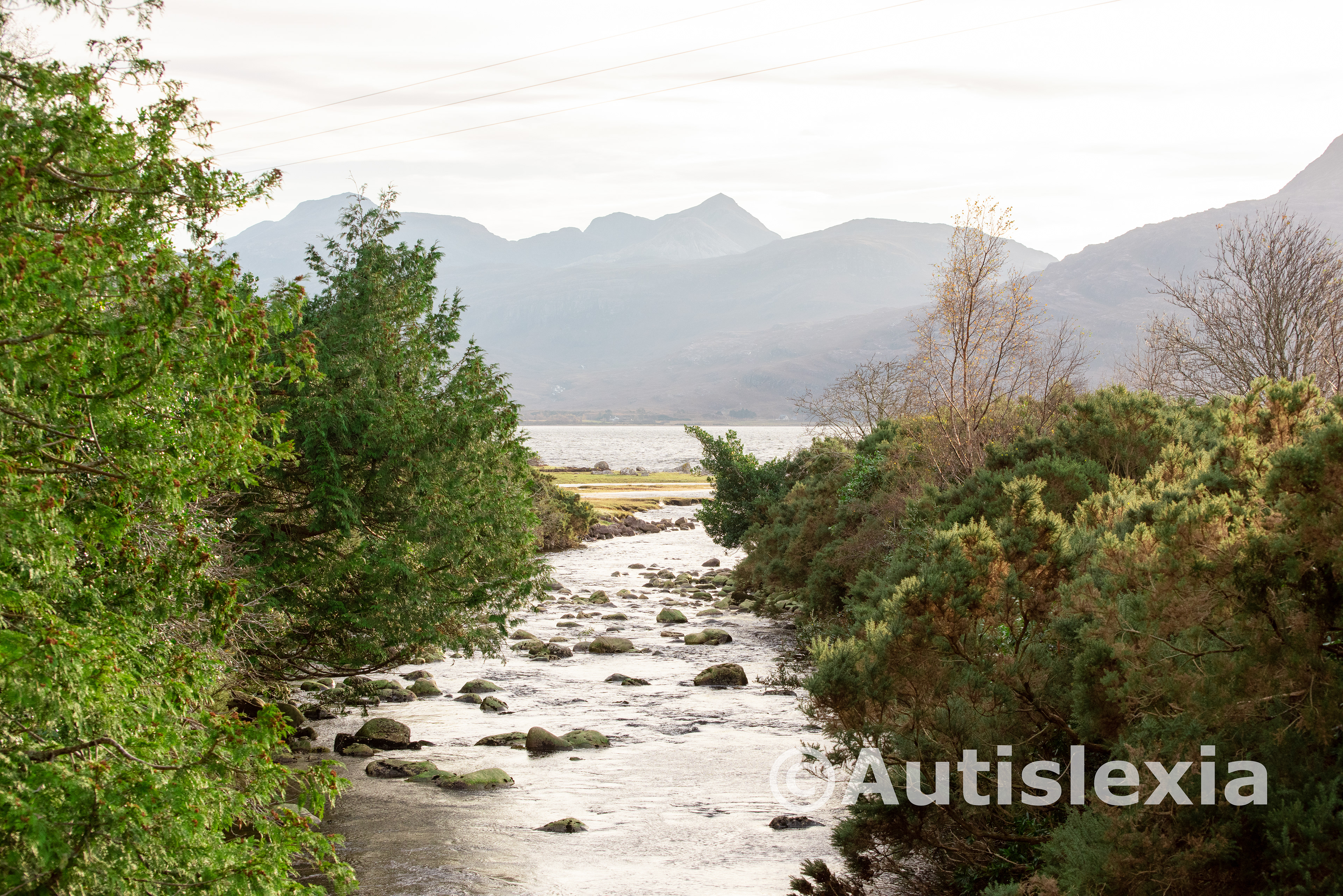 Image of a rocky river flowing into a sea loch with mountains in the distance on the other side of the loch.