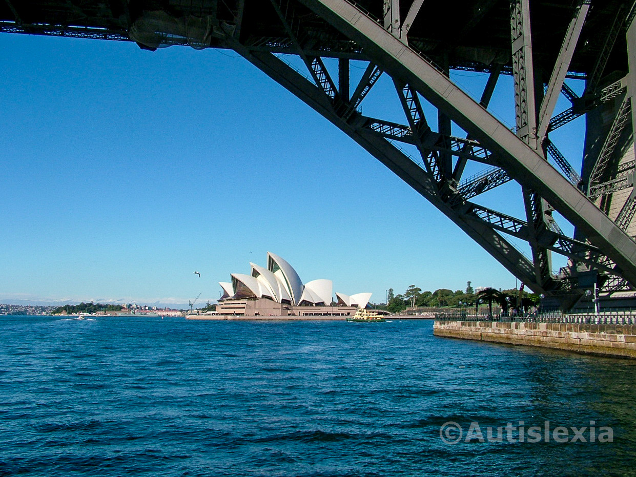 Looking at the side of the Sydney Opera House, from the water with the bottom structure of the Sydney Harbour Bridge dominating the right hand side and the top of the picture.