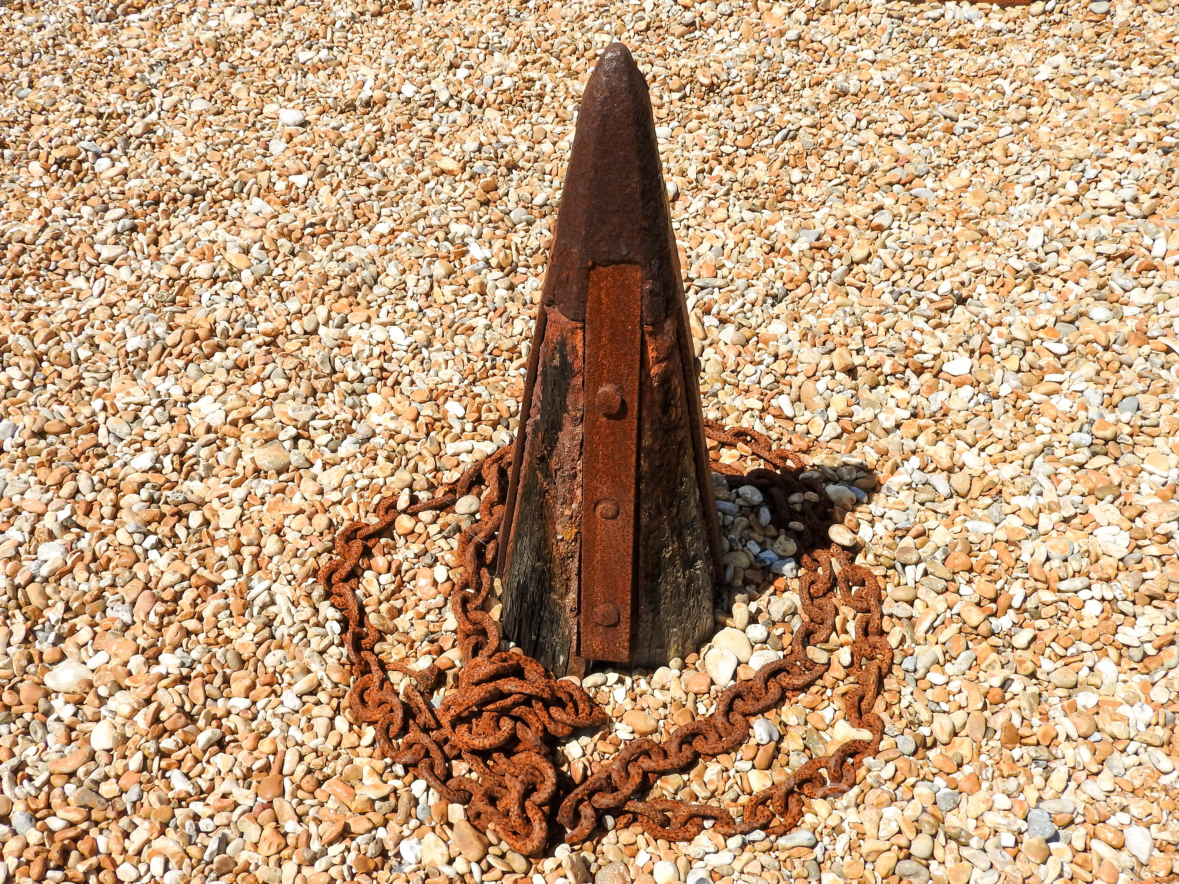 A wooden and rusty metal cone with a rusty chain around it on gravel.