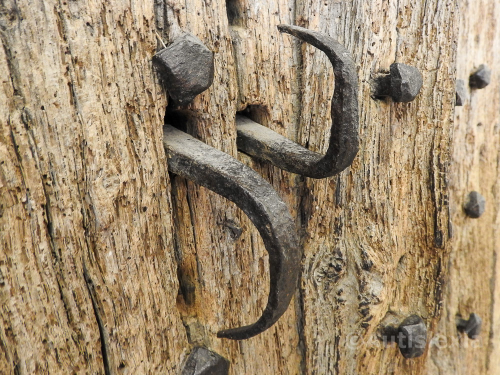 Old metal door latch made of two opposite bent hook shapes, in an old weathered wooden door with iron bolts