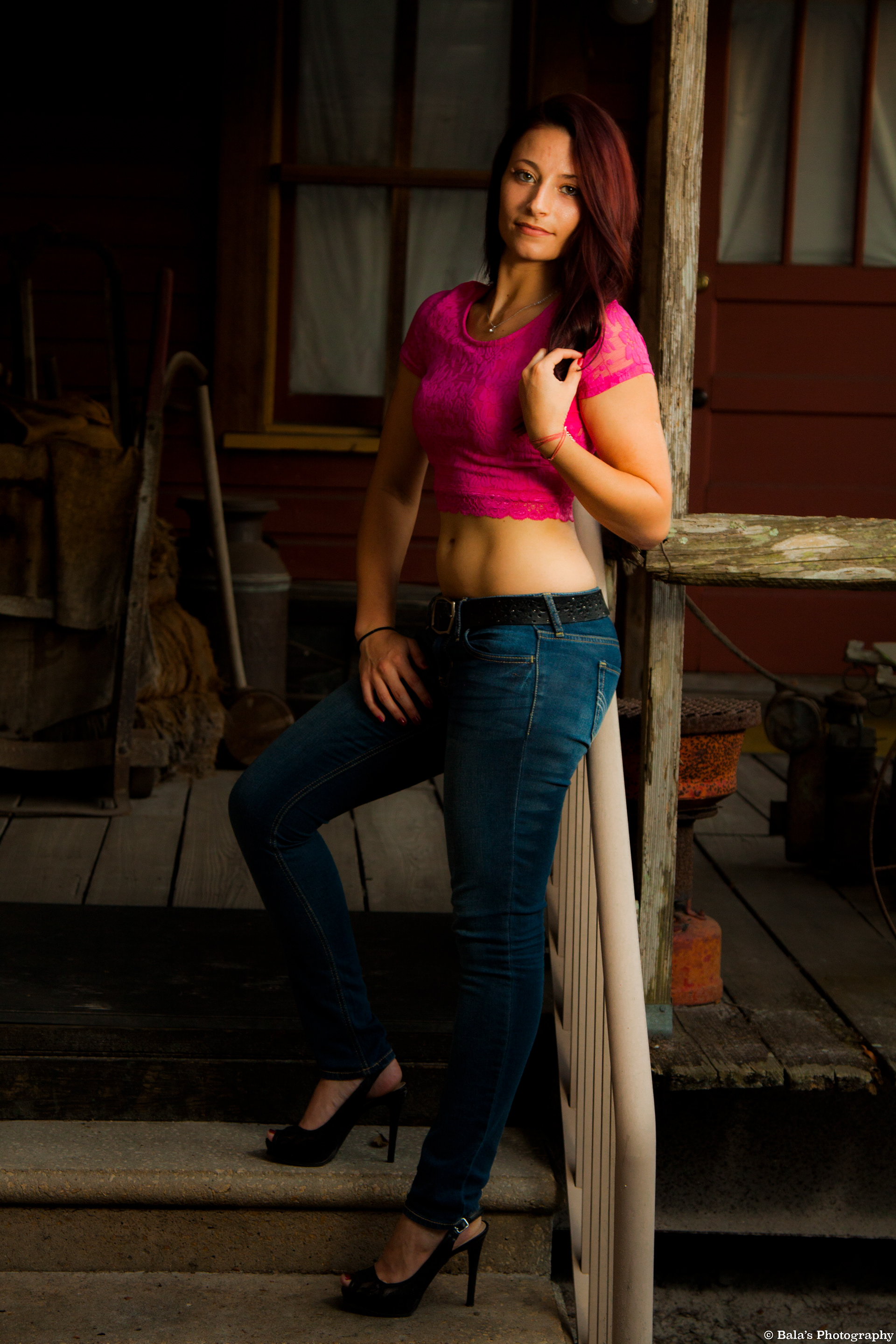 Leaning on the aged rails of a weather-beaten house, she becomes a silent observer of time's passage. The backdrop tells tales of bygone days—wooden echoes, rusted memories, scattered artifacts. In this dance with decay, she lends a touch of grace, a contemporary spirit embraced by the arms of history.
