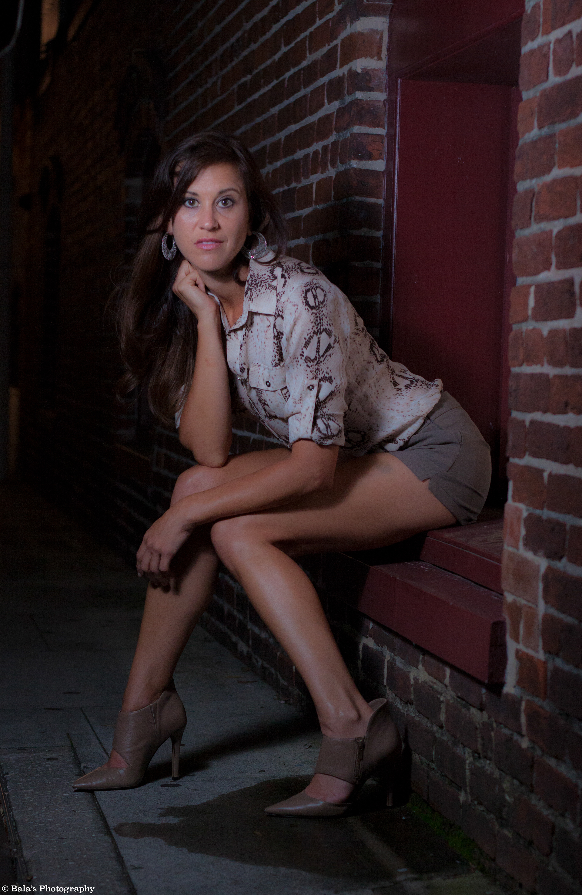Amidst the city lights, she perches by the sidewalk, an enigmatic figure in the night. Her gaze, a beacon of intrigue, adds a touch of allure to the urban landscape, capturing the essence of a city alive with secrets and untold stories.