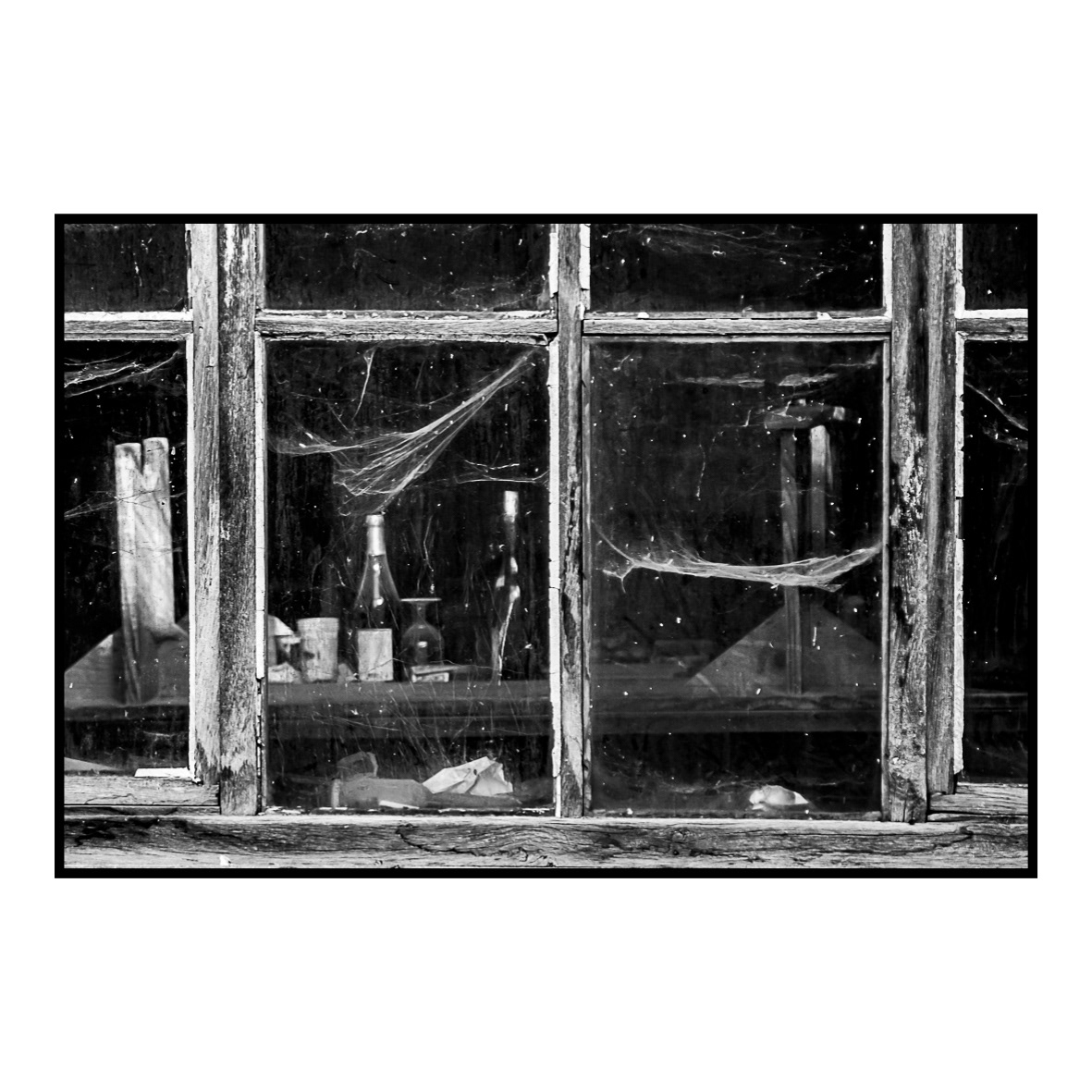 13.	Rayon indiscret (septembre 2011) … lumière sur la vie. Cette image a été réalisée à GIVRAUVAL où j’habite depuis presque vingt ans. De retour d’une promenade en forêt (sans appareil photo), je passe devant cet ancien atelier où les aînés du village ont pris l’habitude de venir jouer aux cartes les après-midis tout en sirotant quelques verres de vin. Ce jour-là, la matinée est douce et le soleil déjà haut dans le ciel vient frapper de ses rayons la fenêtre principale qui donne sur la rue. La lumière qui pénètre dans la pièce révèle une scène absolument incroyable ! Mais comment peut-il y avoir de la vie ici avec cette fenêtre couverte de toiles d’araignées ? Pourtant, c’est un lieu incontournable du village, où se mêlent bonne humeur, convivialité et discussions passionnées. Quatre-à-quatre, je cours chercher mon boîtier pour photographier l’endroit. A mon retour, je fais volontairement la mise au point sur la fenêtre afin de plonger légèrement l’arrière-plan dans le flou. J’incite ainsi le spectateur à promener son regard dans toute l’image à la recherche d’indices puis à se questionner sur la fonction de ce lieu. Pas simple ! Cet endroit a d’ailleurs trouvé depuis quelques années une nouvelle utilisation en devenant l’atelier communal où résonnent encore éclats de rires et tintements de verres.