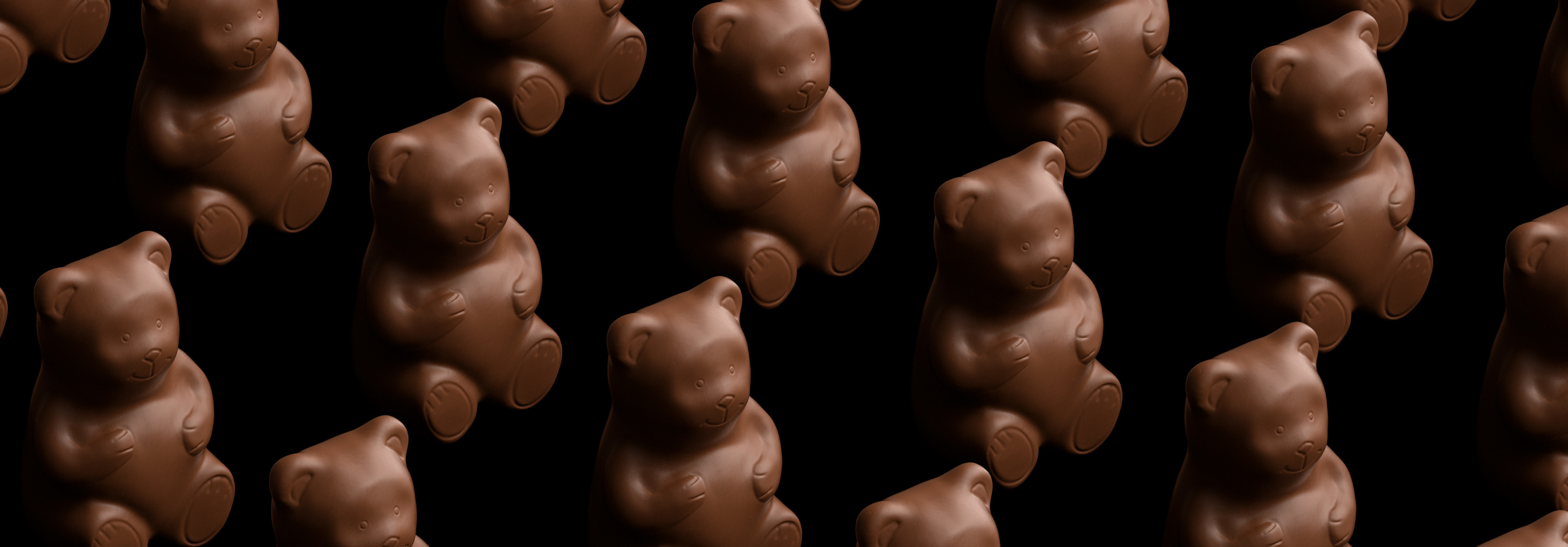 Multiple chocolate bear figurines arranged in a pattern against a black background, showcasing their smooth and detailed design.