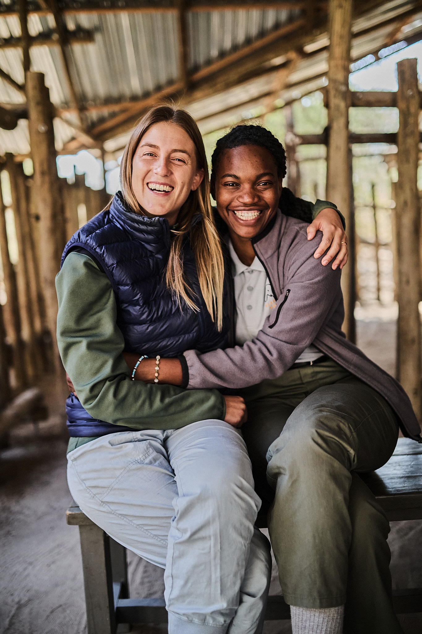 Two women laughing and embracing on a bench in Botswana, from the documentary Coexistence