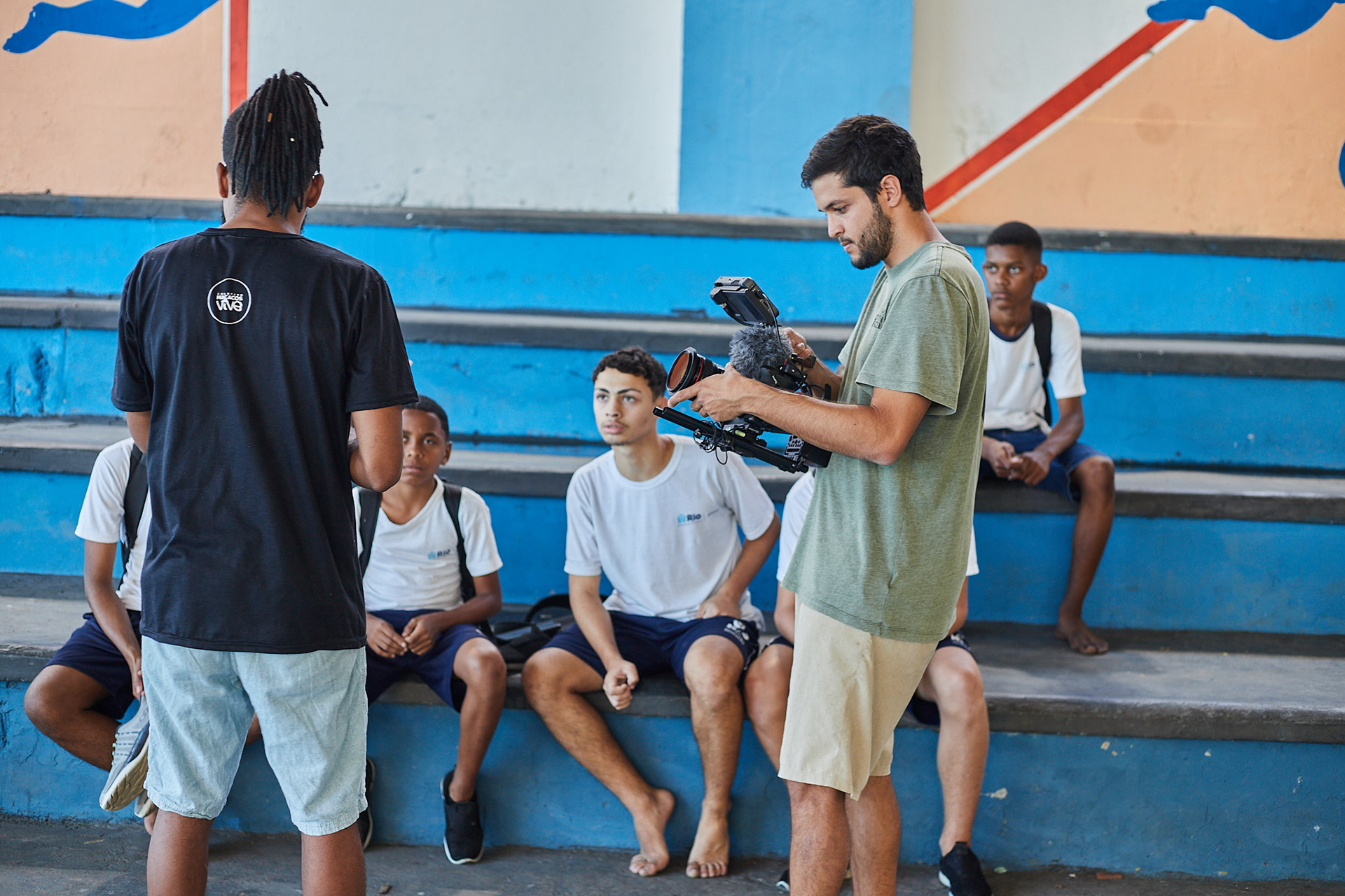 Behind the scenes: a filmmaker with a camera films young football players and their coach in the stands of a Rio de Janeiro court, for the documentary Macacos Vive
