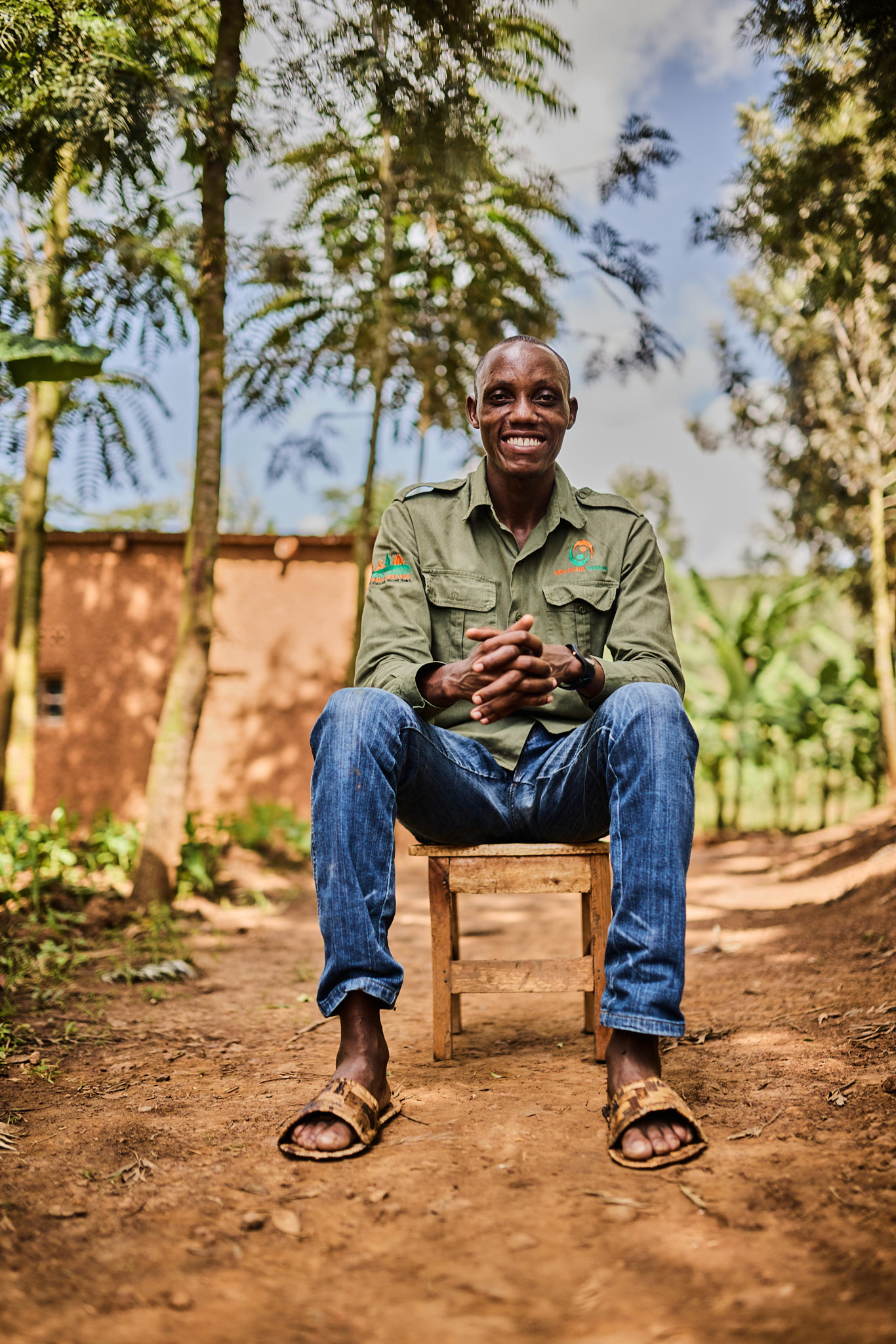 John, the young Rwandan entrepreneur who turns banana husks into sandals, smiling on a wooden stool, from the documentary Ni Maisha