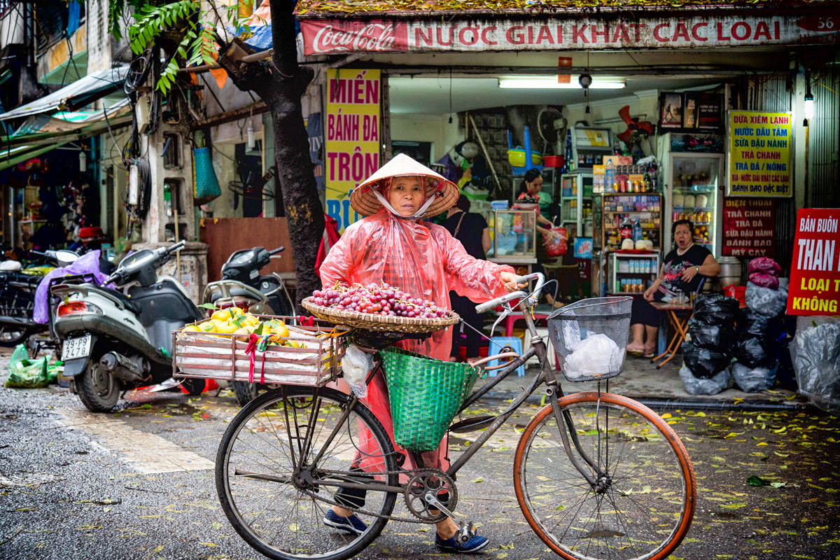 A woman pushes her bicycle through a market area in Hanoi, Vietnam