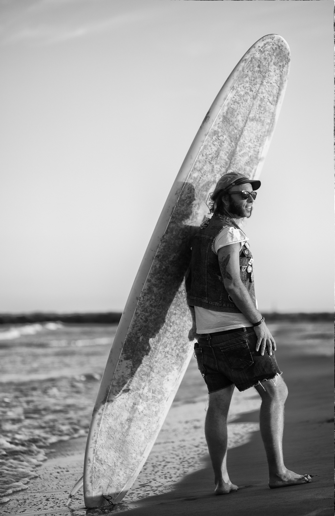 fotografía en blanco y negro de un surfista en la playa con la tabla en la espalda