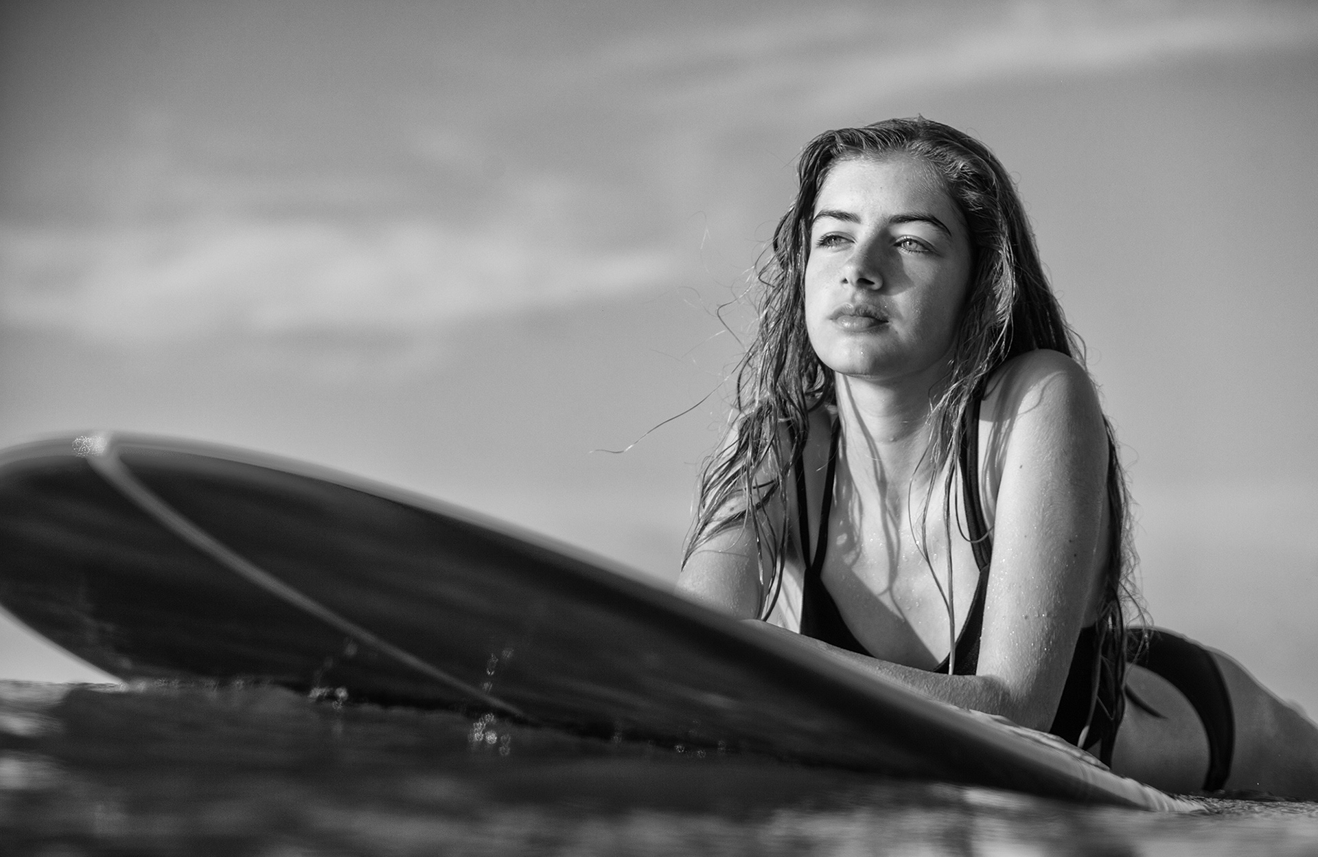 fotografía en blanco y negro de una surfista flotando en el mar encima de una tabla