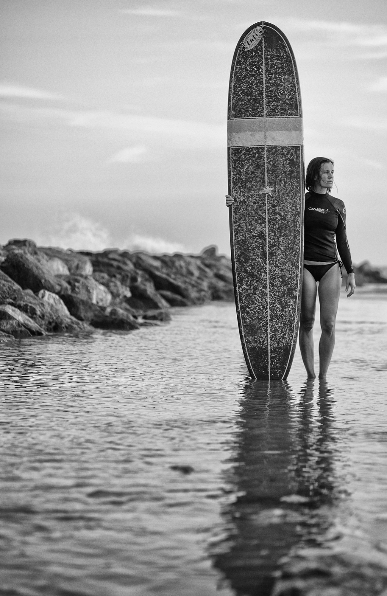 Fotografía de una surfista de pie en la playa con la tabla a su lado 