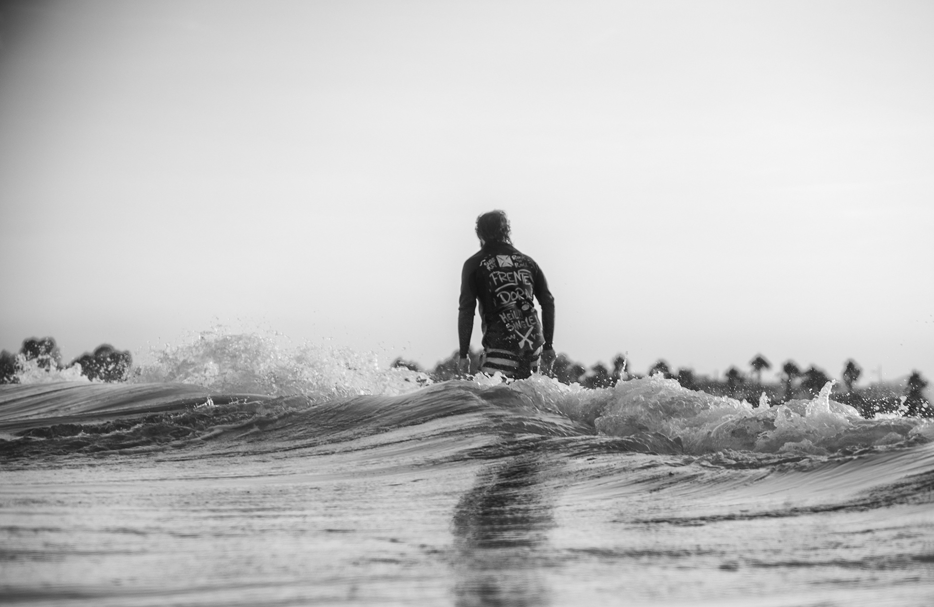Fotografía en blanco y negro de un surfista surfeando una ola de espaldas