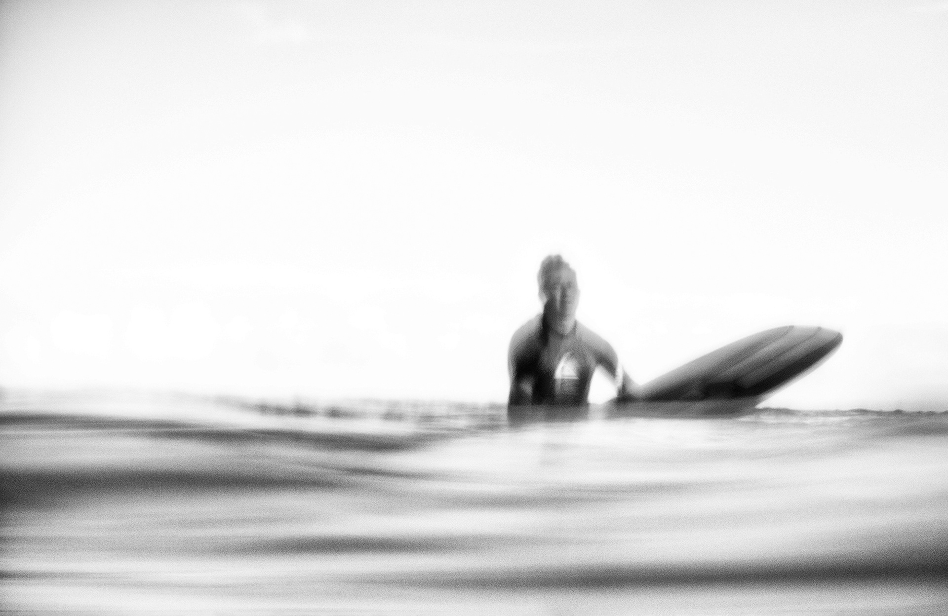 Retrato desenfocado en blanco y negro de un surfista flotando en el mar con una tabla