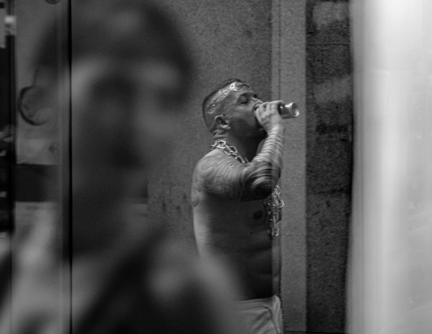 A solitary figure, lost in thought, drinks beneath a crown of laurels — a fleeting king in the anonymity of the streets. The blurred onlooker gazes through the glass, connecting their worlds for an instant. In this layered reflection, the boundary between ruler and observer blurs, hinting at the hidden stories we carry beneath our public facades.