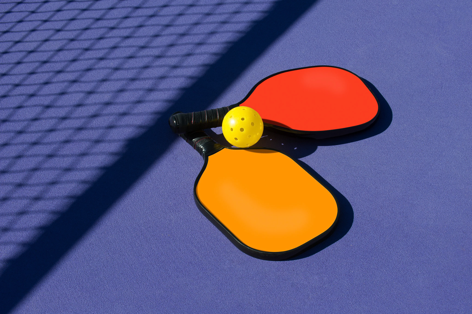Two paddles and ball sitting near net shadow       