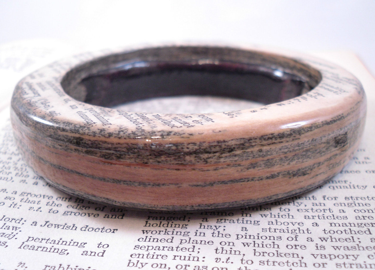 This piece is made from layered pages of a 1937 Webster’s Dictionary that I discovered in a thrift store, a vintage book that most likely would have been thrown away. Instead of letting it be discarded, I gave it new life as a wearable piece of art.  The nearly 90-year-old pages are fused together and wrapped in brown leather, then hardened until they feel solid like wood, a nod to paper’s original source. Small openings reveal my signature and the layered edges of the pages, and a clear gloss finish seals and protects the piece.  Each bangle takes up to eight weeks to complete. I love transforming something overlooked into something lasting and meaningful.