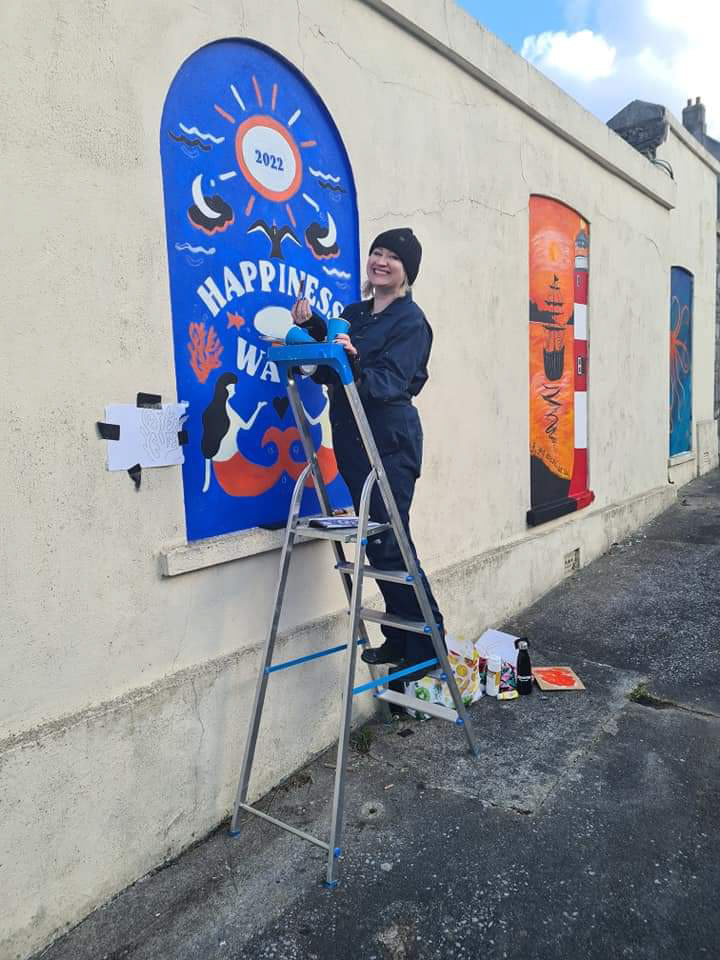Serena June Horgan on a ladder painting a mural