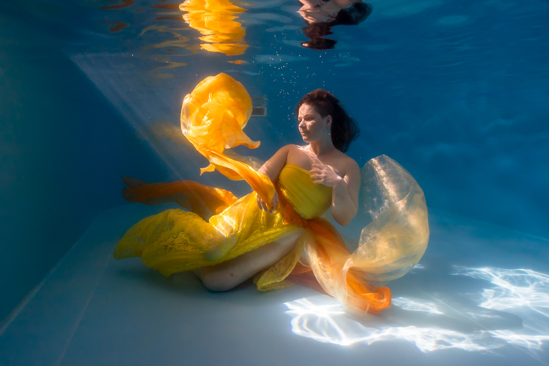 Žena ve žlutých šatech pod vodou při módním focení