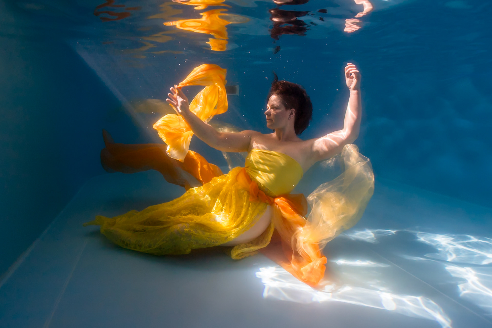 Žena ve žlutých šatech pod vodou při módním focení