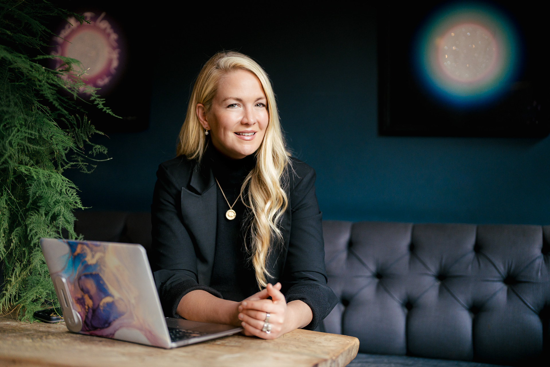 blonde lady sitting with open laptop on a dark background, example of contemporary business portrait headshots