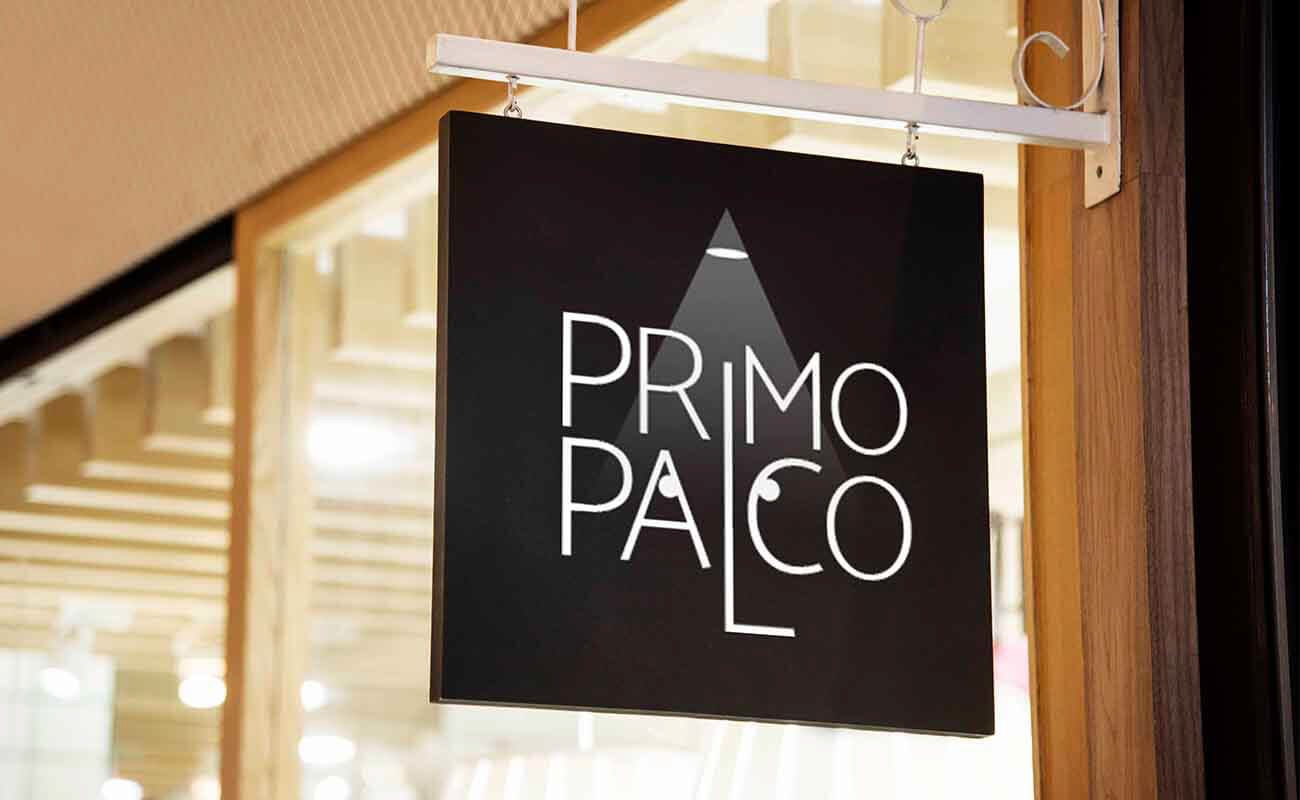 Primo Palco logo designed by graphic designer Darka White, displayed on a sign in front of a theater, featuring a spotlight as the dot on the 'I' and eyes within the 'a' and 'c' of 'palco' to symbolize stage visibility for young talents.