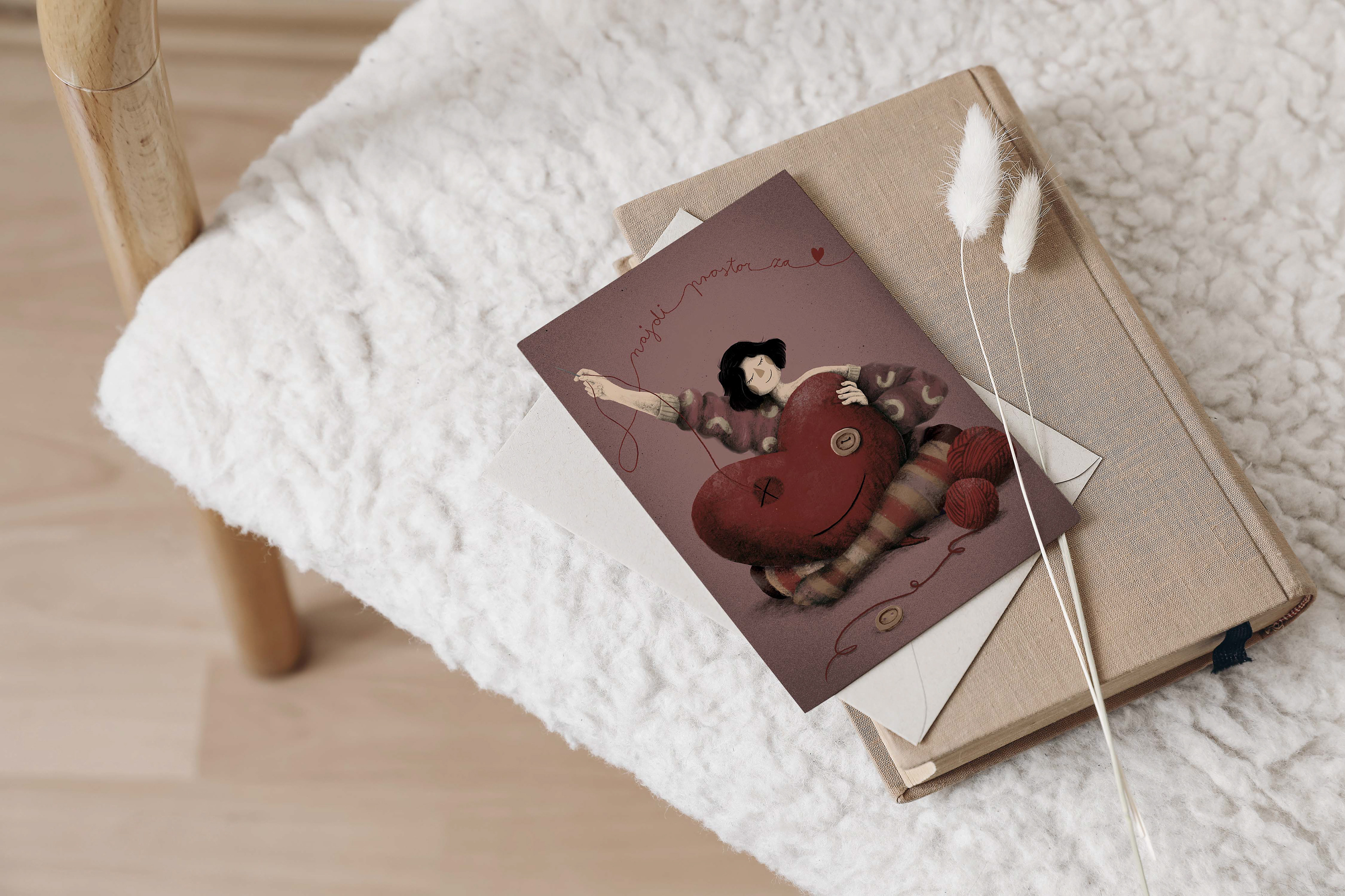 Postcard featuring an illustrated woman sewing a large red heart, placed on a soft textured chair next to a book and dried flowers. The card displays the words 'najdi prostor za' written with red thread in cursive, creating a cozy and inviting scene with a handmade vibe. Illustration by Darka White Art