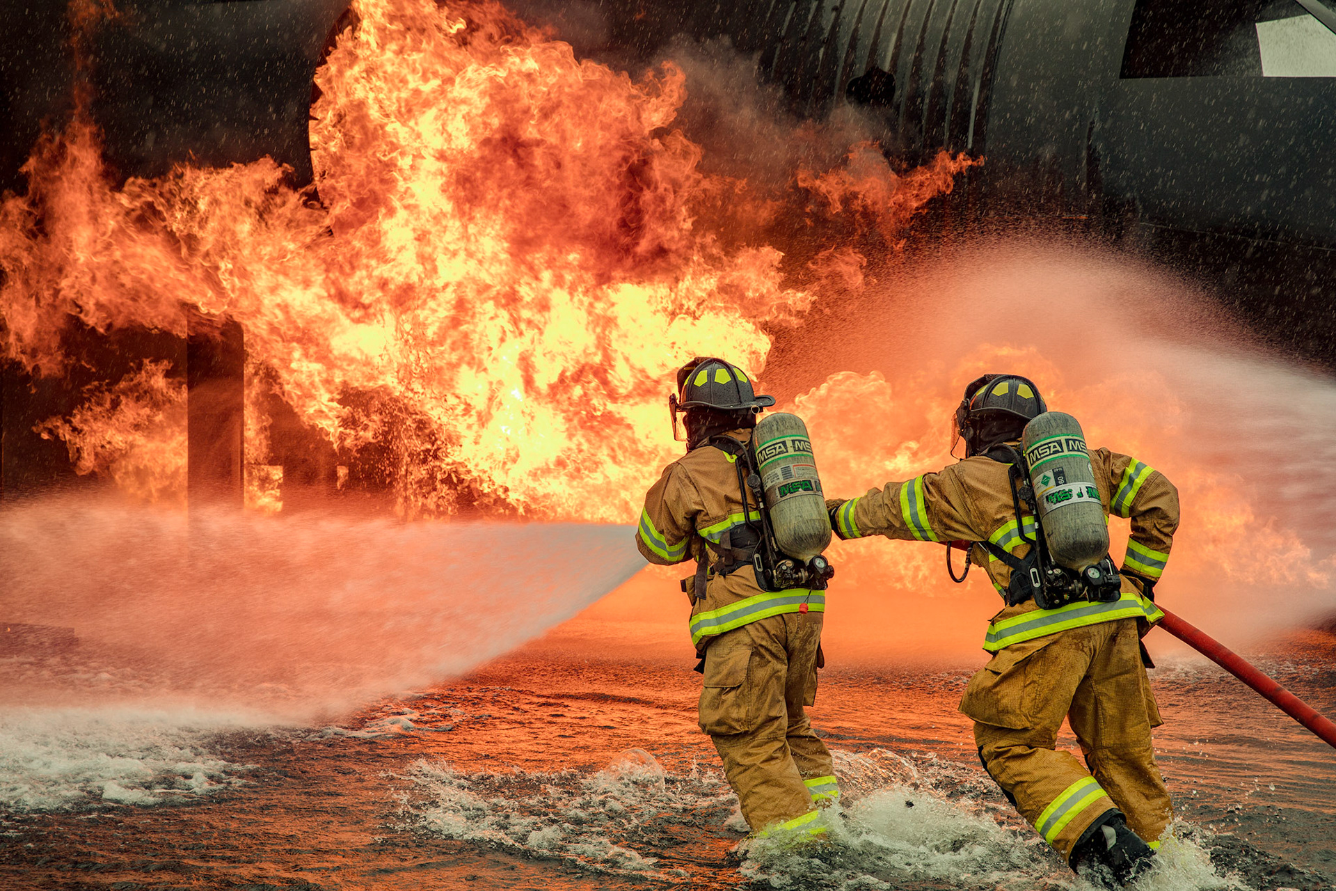A two-person fire attack crew with the 374th Civil Engineer Squadron fire and emergency services flight, aim a stream of water on a simulated aircraft fire at Yokota Air Base, Japan, March 8, 2018. Aircraft live-fire training is conducted periodically throughout the year to ensure Airmen and civilians with the 374th CES and 374th Maintenance Squadron repair and reclamation section are always prepared to combat aircraft fuel fires. (U.S. Air Force photo by Yasuo Osakabe)