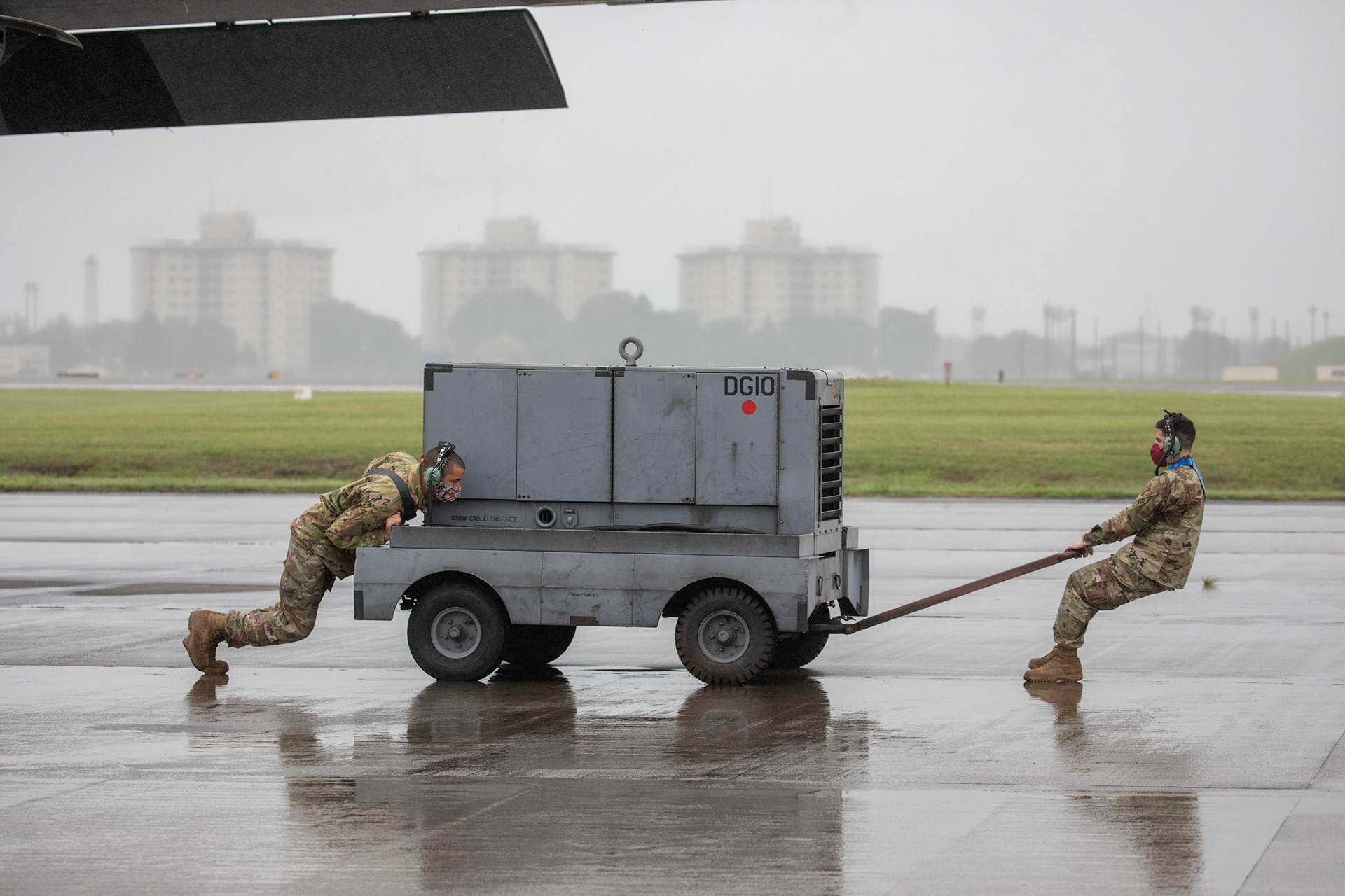 Crew chiefs assigned to the 374th Aircraft Maintenance Squadron push an A/M32 diesel generator into position prior to starting a C-130J Super Hercules during the Samurai Surge training exercise at Yokota Air Base, Japan, May 21, 2020. To ensure the health and safety of its Airmen in the face of an ongoing COVID-19 pandemic, Yokota’s personnel proactively utilize social distancing and cloth face coverings to better protect themselves, the community, and the Wing’s overall mission capability.(U.S. Air Force photo by Yasuo Osakabe)