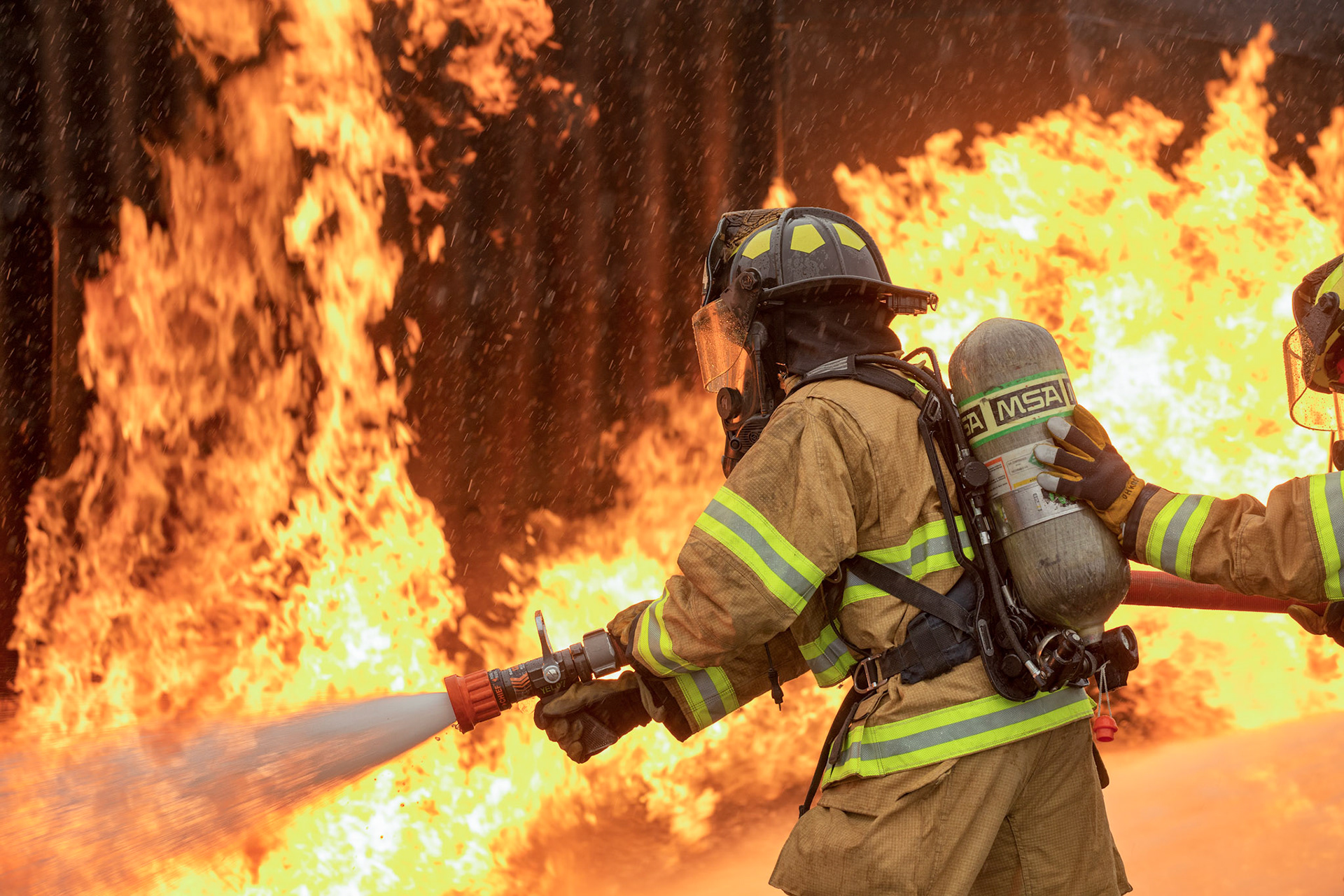 A two-person fire attack crew with the 374th Civil Engineer Squadron fire and emergency services flight, aim a stream of water on a simulated aircraft fire at Yokota Air Base, Japan, March 8, 2018. Aircraft live-fire training is conducted periodically throughout the year to ensure Airmen and civilians with the 374th CES and 374th Maintenance Squadron repair and reclamation section are always prepared to combat aircraft fuel fires. (U.S. Air Force photo by Yasuo Osakabe)